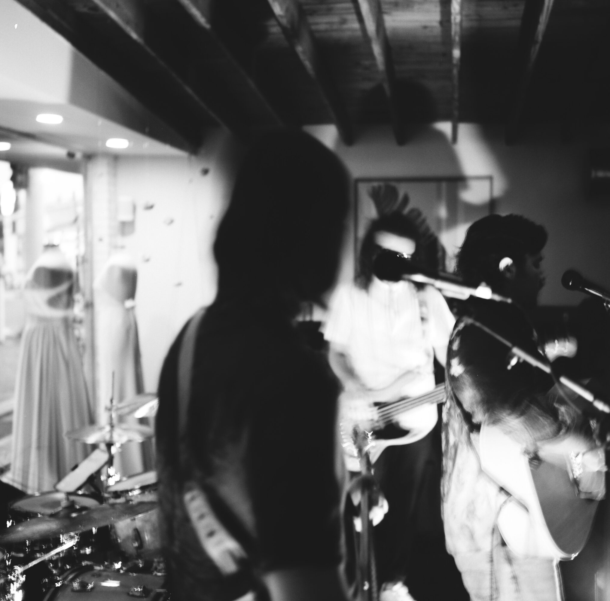 Band performing with microphones and instruments in a dimly lit indoor space.