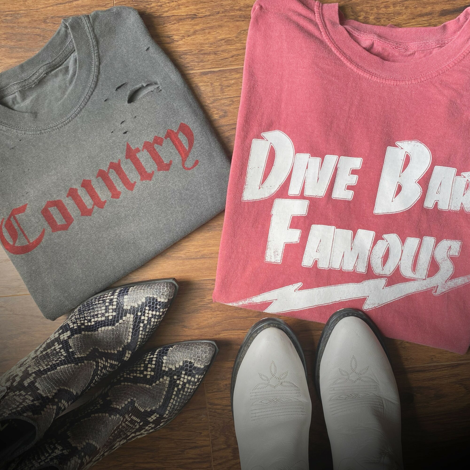 Gray sweatshirt with red text, pink sweatshirt with white text, snake-patterned shoes, and white shoes on wooden surface.