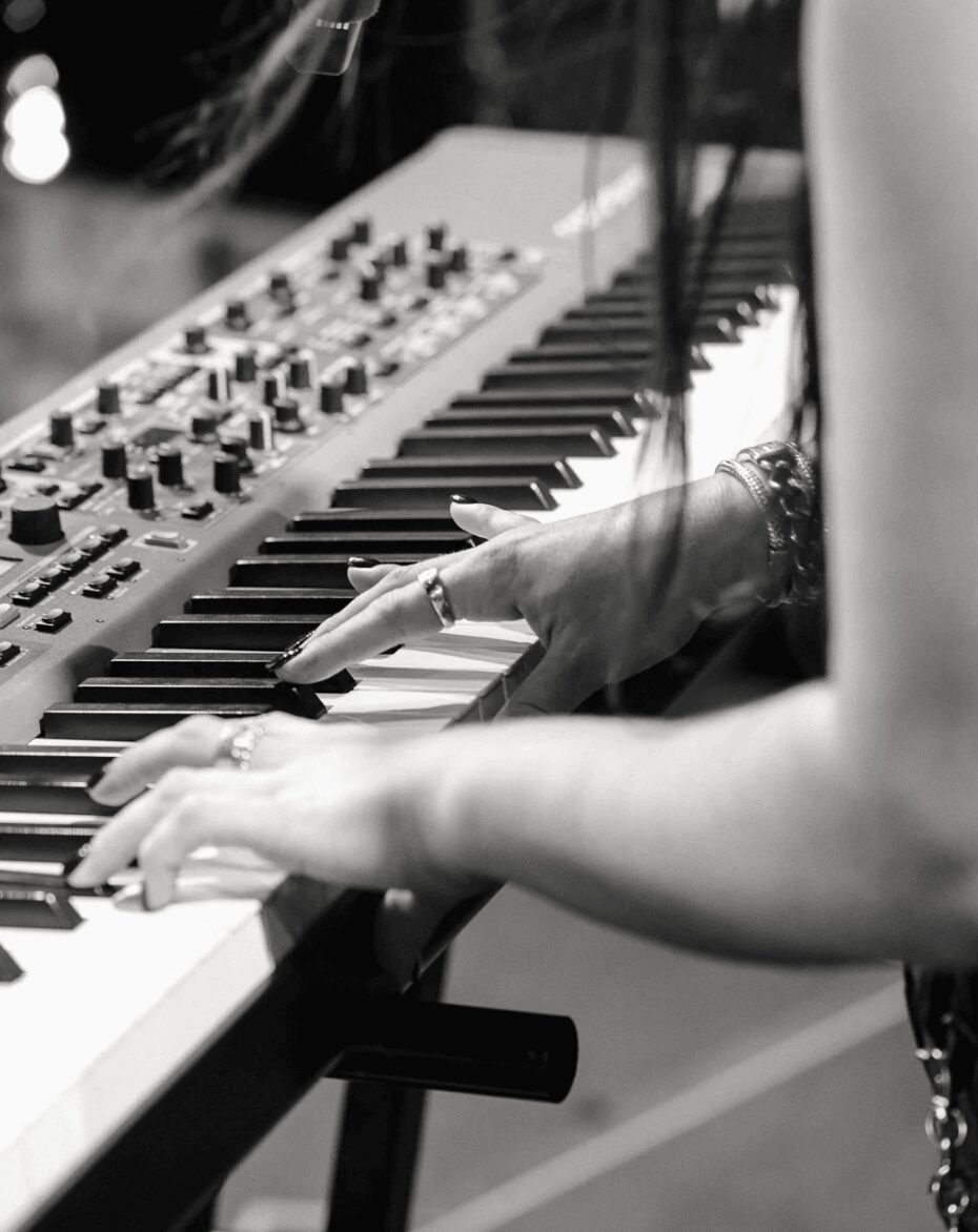 Person's hand playing a keyboard with a synthesizer, focus on fingers and instrument, black and white photo.