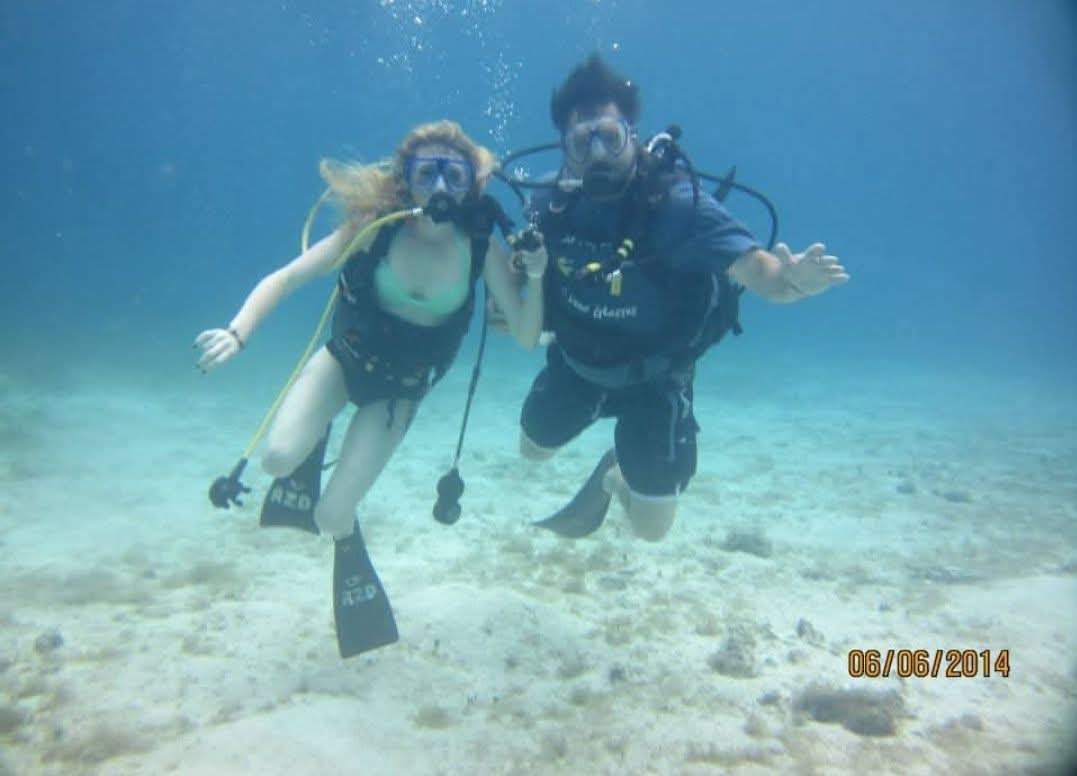 Two people scuba diving underwater, holding hands, with sandy ocean floor visible, date 08/05/2014.