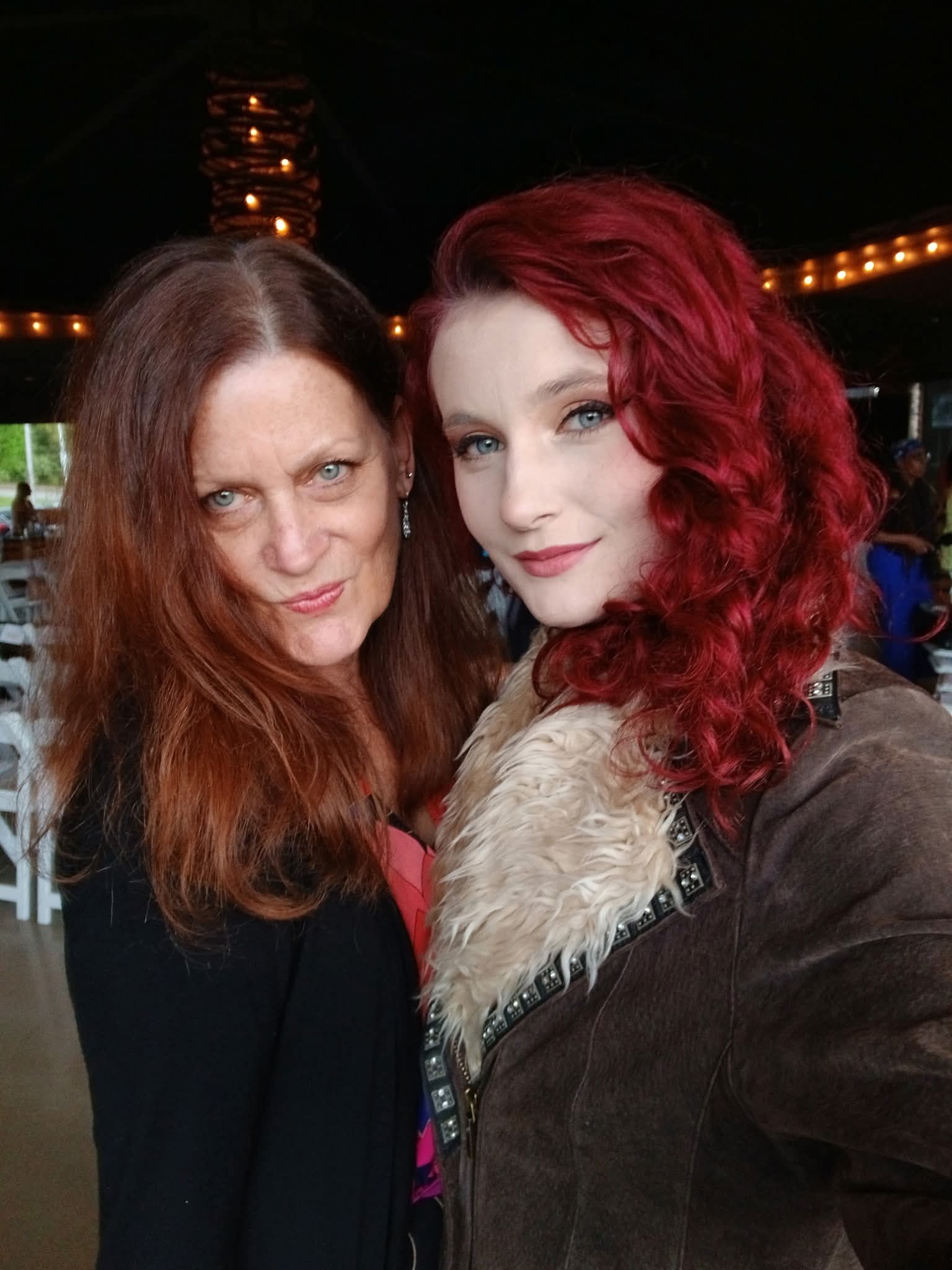 Two women with red hair posing together indoors, smiling at the camera.