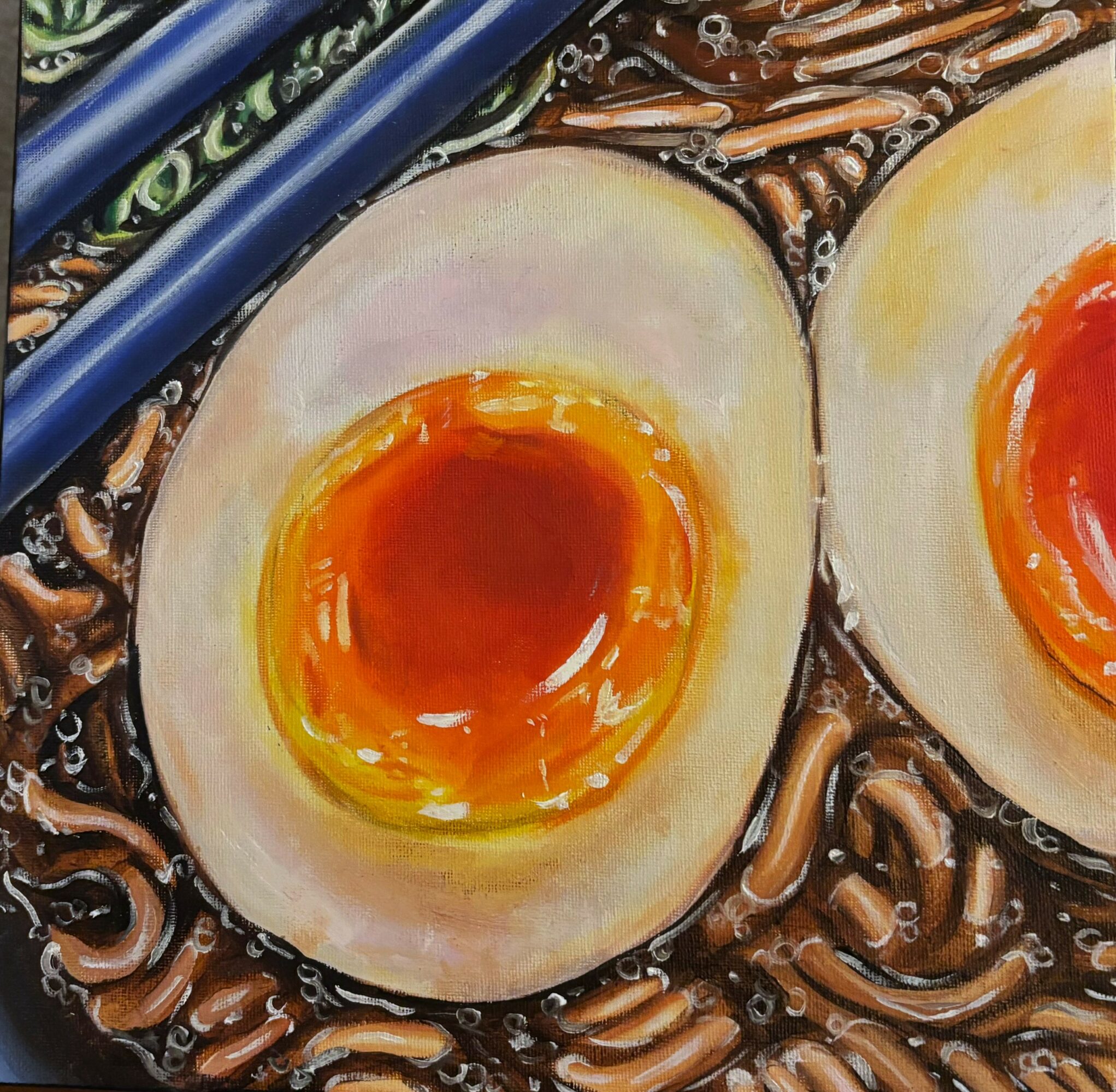 Close-up of halved soft-boiled eggs with runny yolks on a bed of noodles, with a blue utensil nearby.