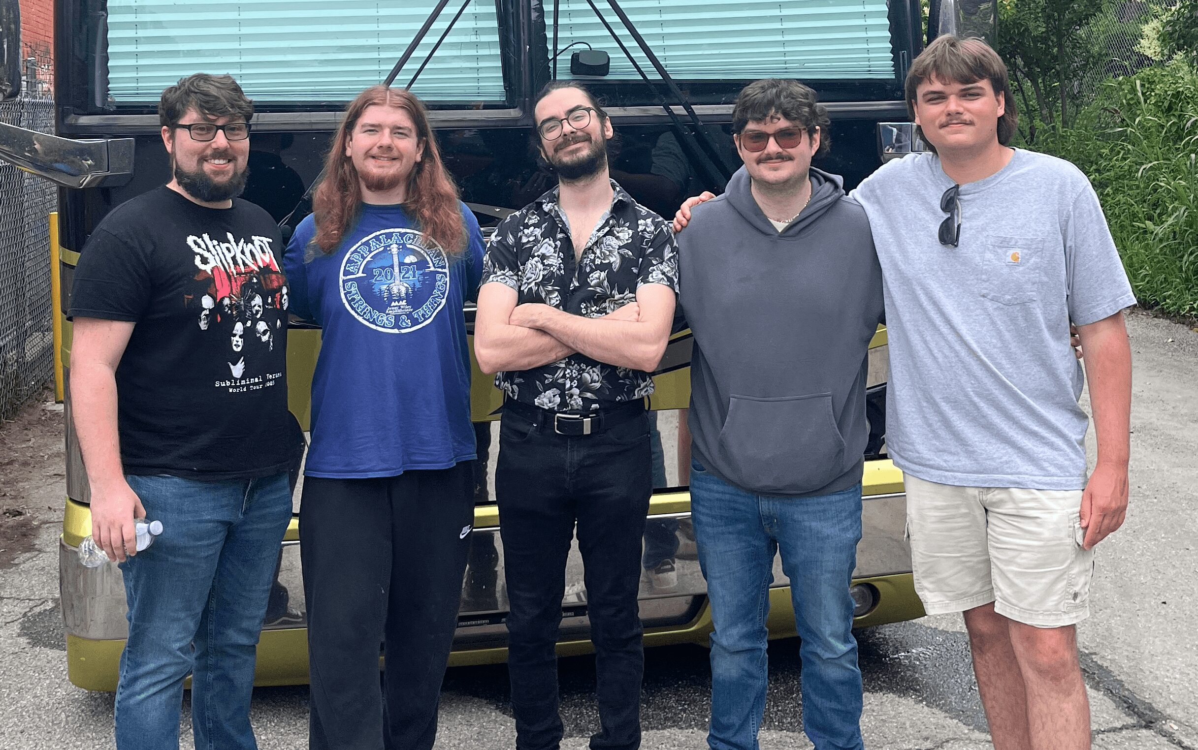 Five people stand outdoors in front of a vehicle, smiling and posing for the photo.