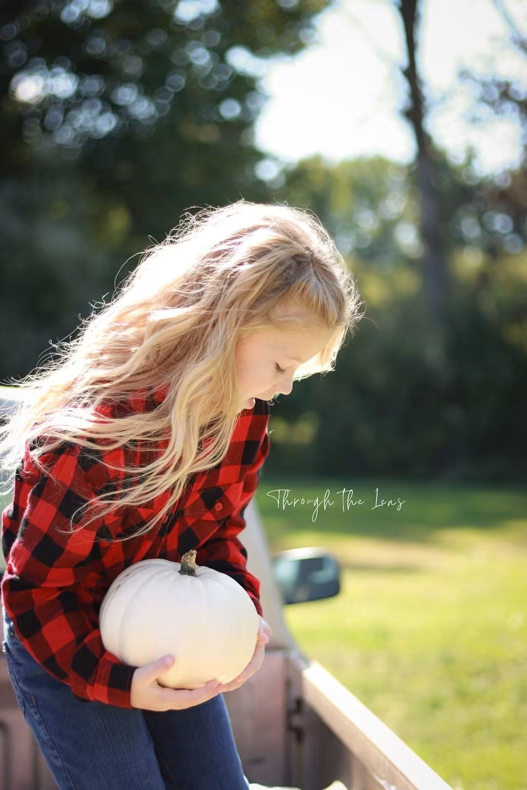 Young girl with long blonde hair holding a white pumpkin outdoors on a sunny day.