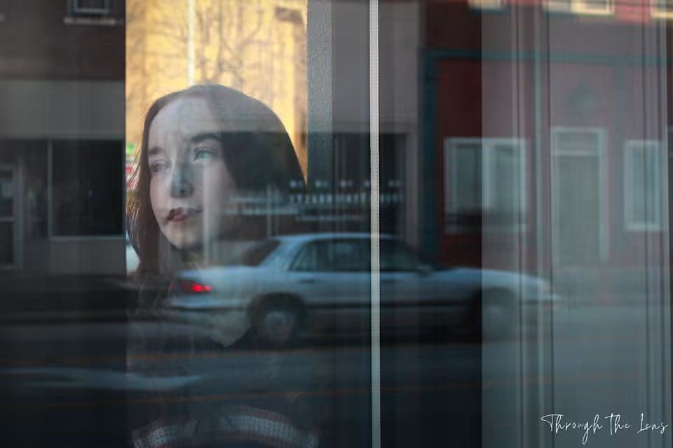Reflection of a woman's face in a glass window with a street scene behind her.