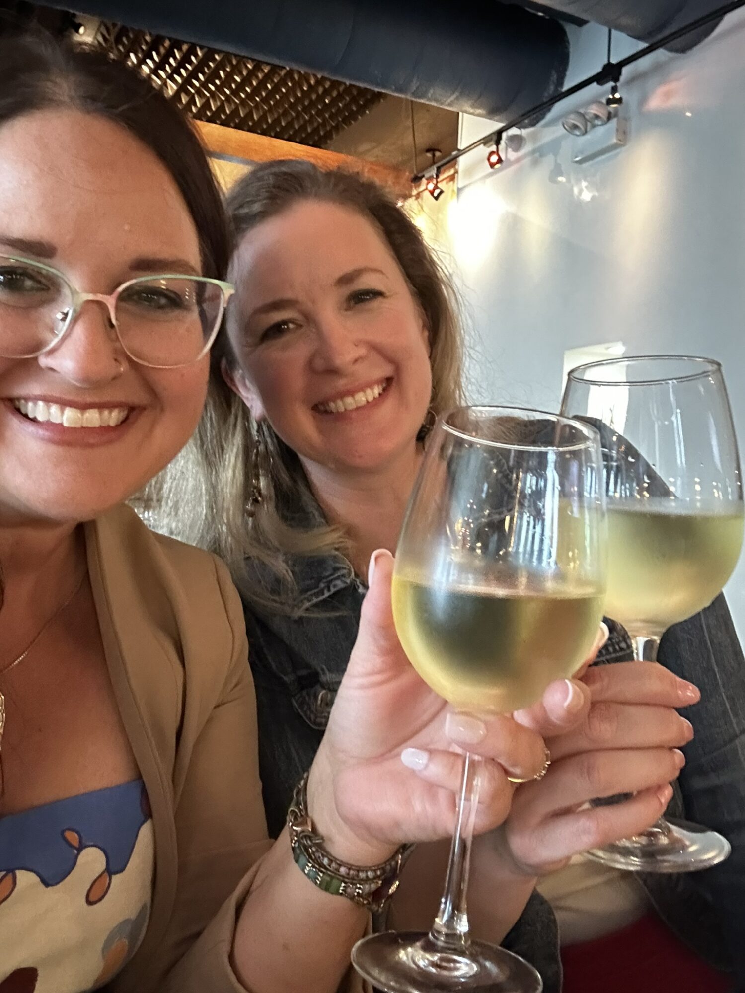Two women smiling and holding glasses of white wine at a celebration or gathering.