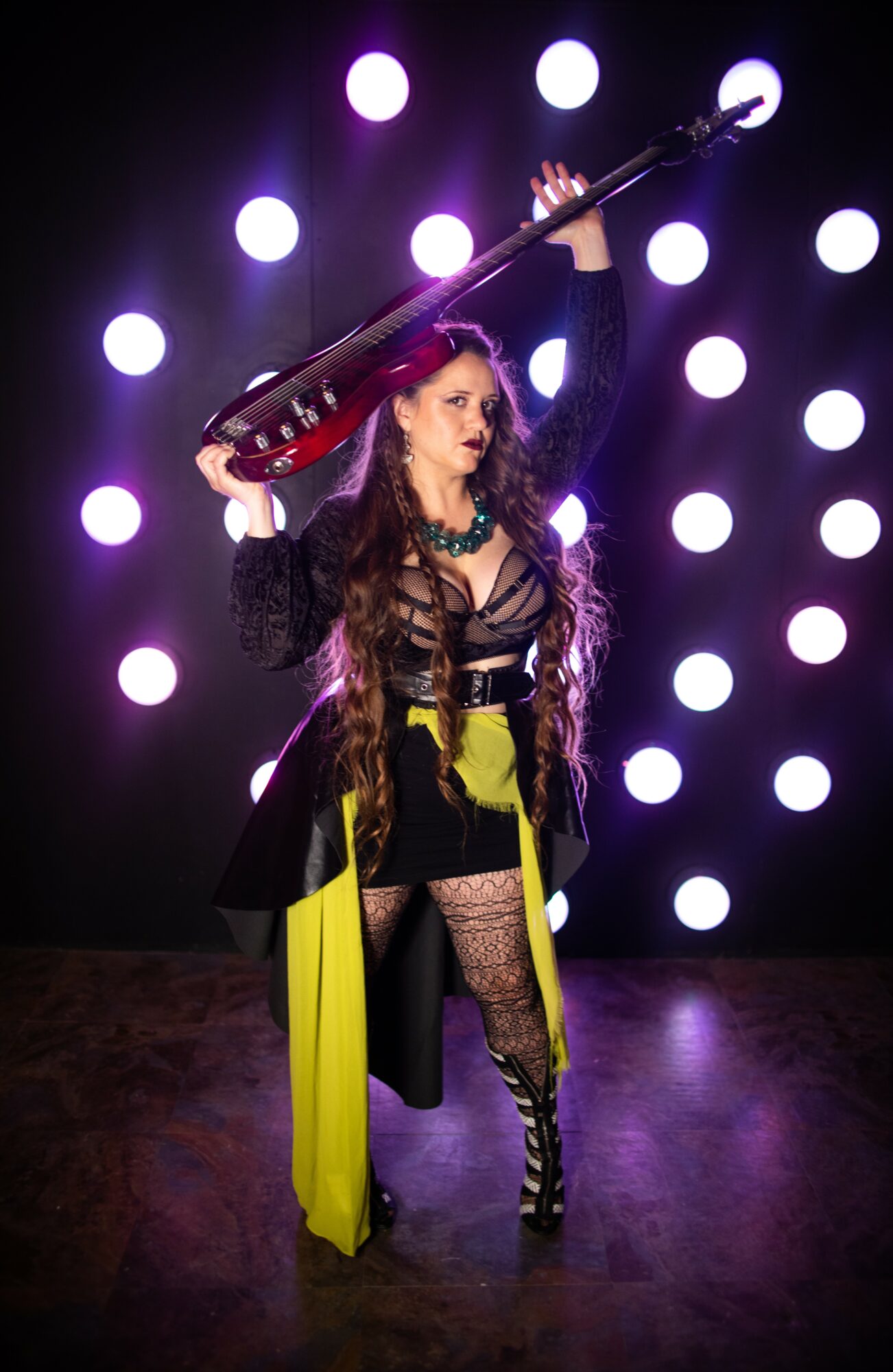 Woman with long hair holding a guitar above her head, stage lights in background