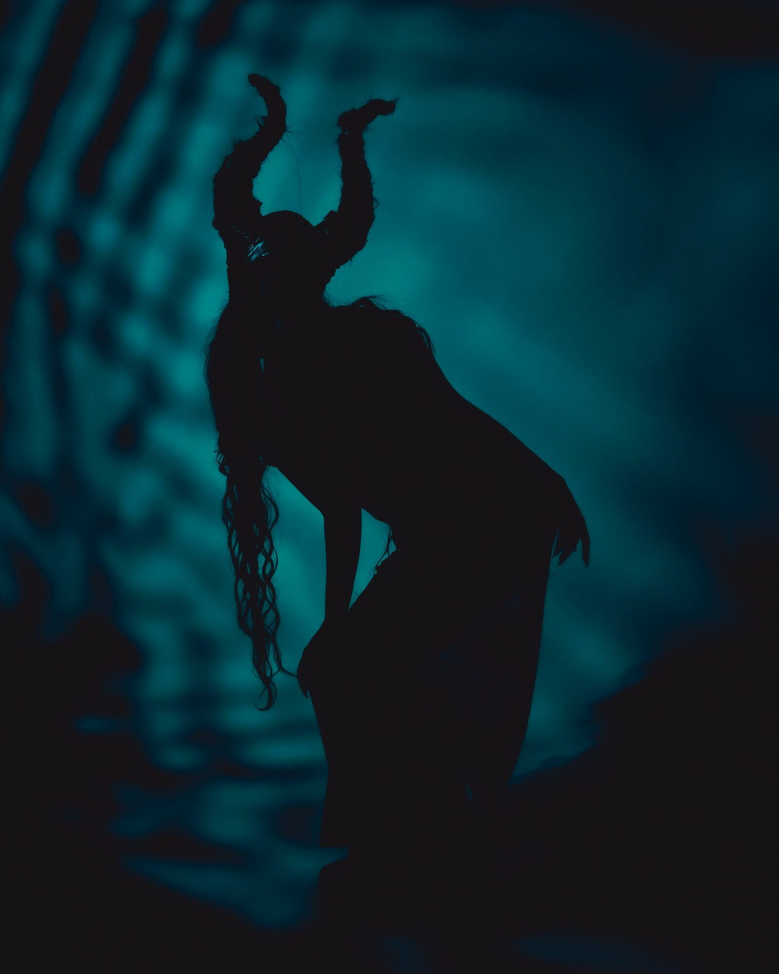 Silhouette of a person with arms raised, long hair, against a blue background with light patterns.