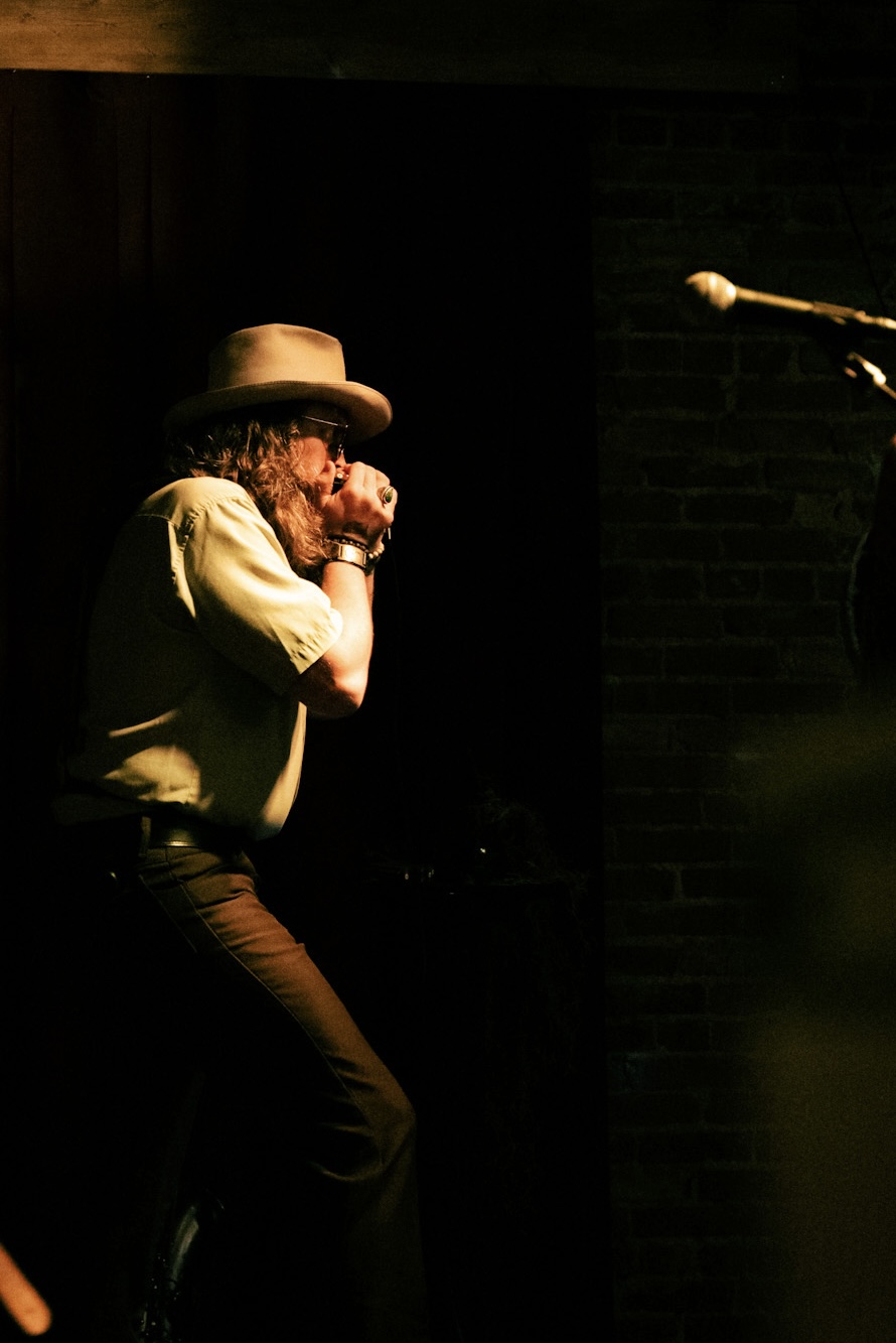 Person wearing a hat and yellow shirt, standing near a microphone, in a dimly lit setting.