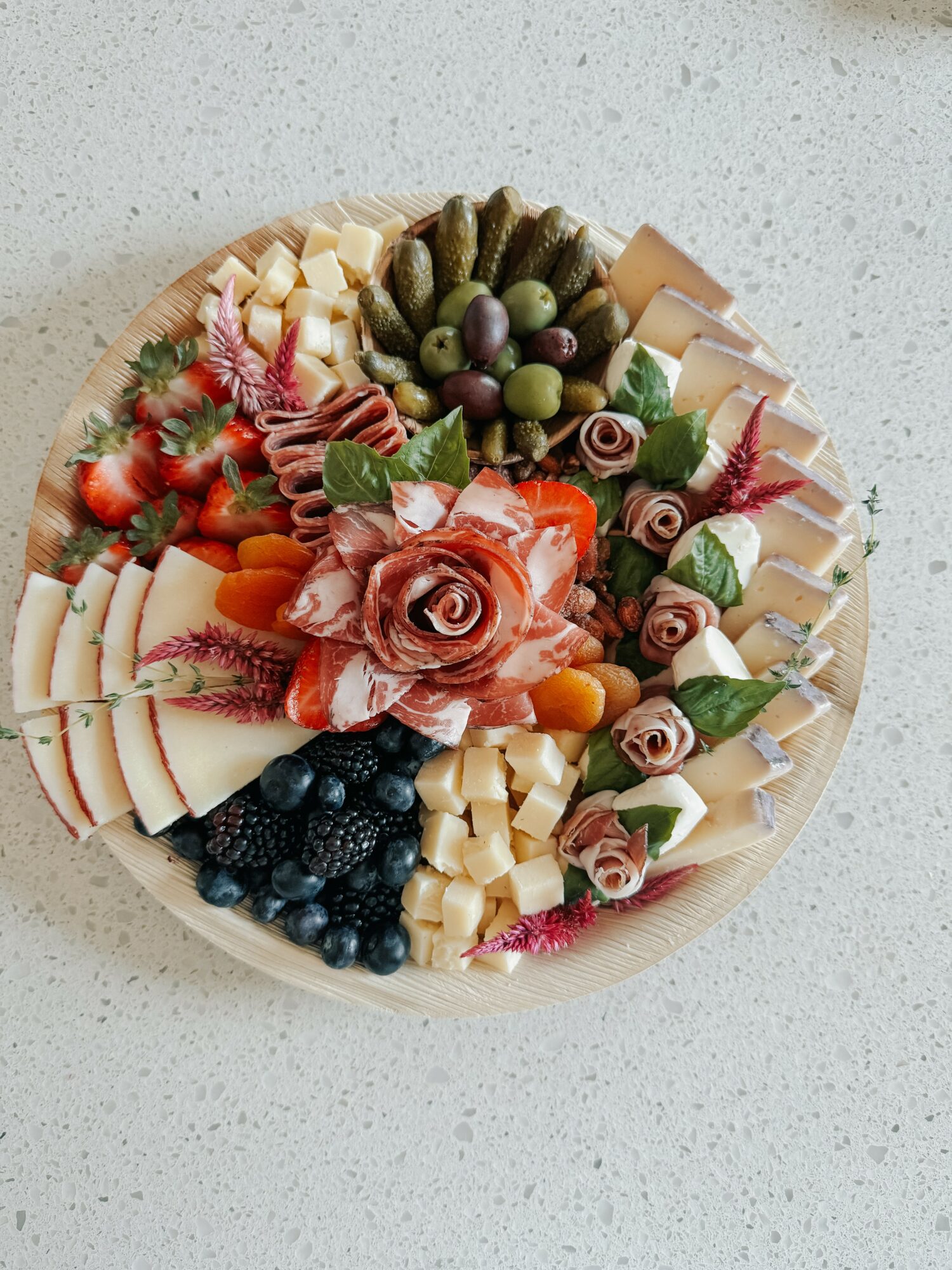Round cheese and fruit platter with grapes, strawberries, blueberries, and decorative rose-shaped cheese pieces, on a light surface.