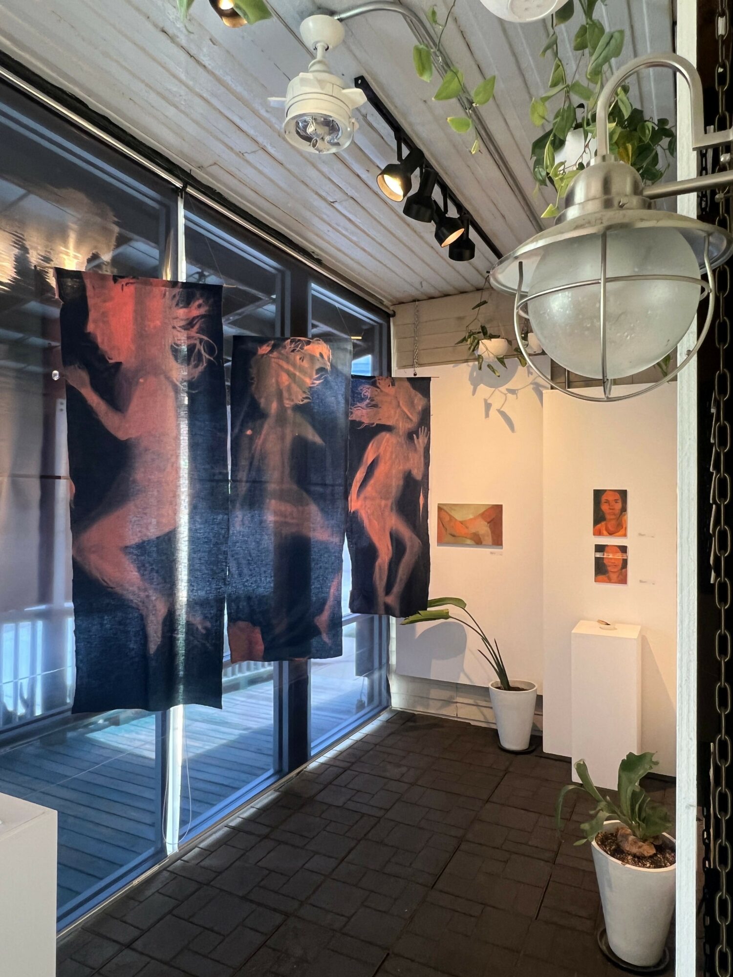 Balcony with hanging curtains, potted plants, and artwork on the wall, viewed from the side.