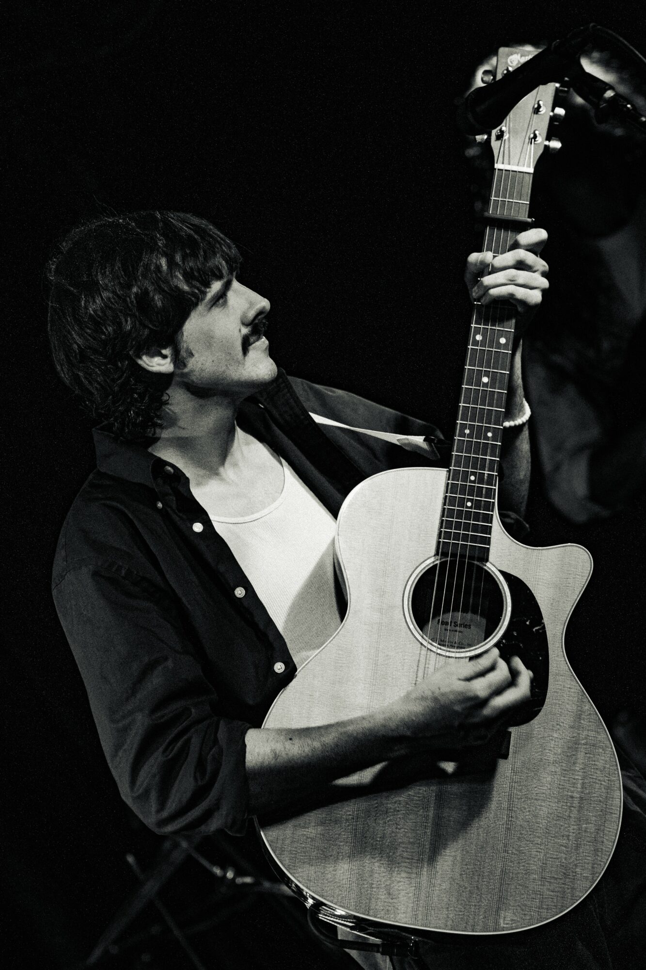 Person holding an acoustic guitar, looking at it, in black and white.
