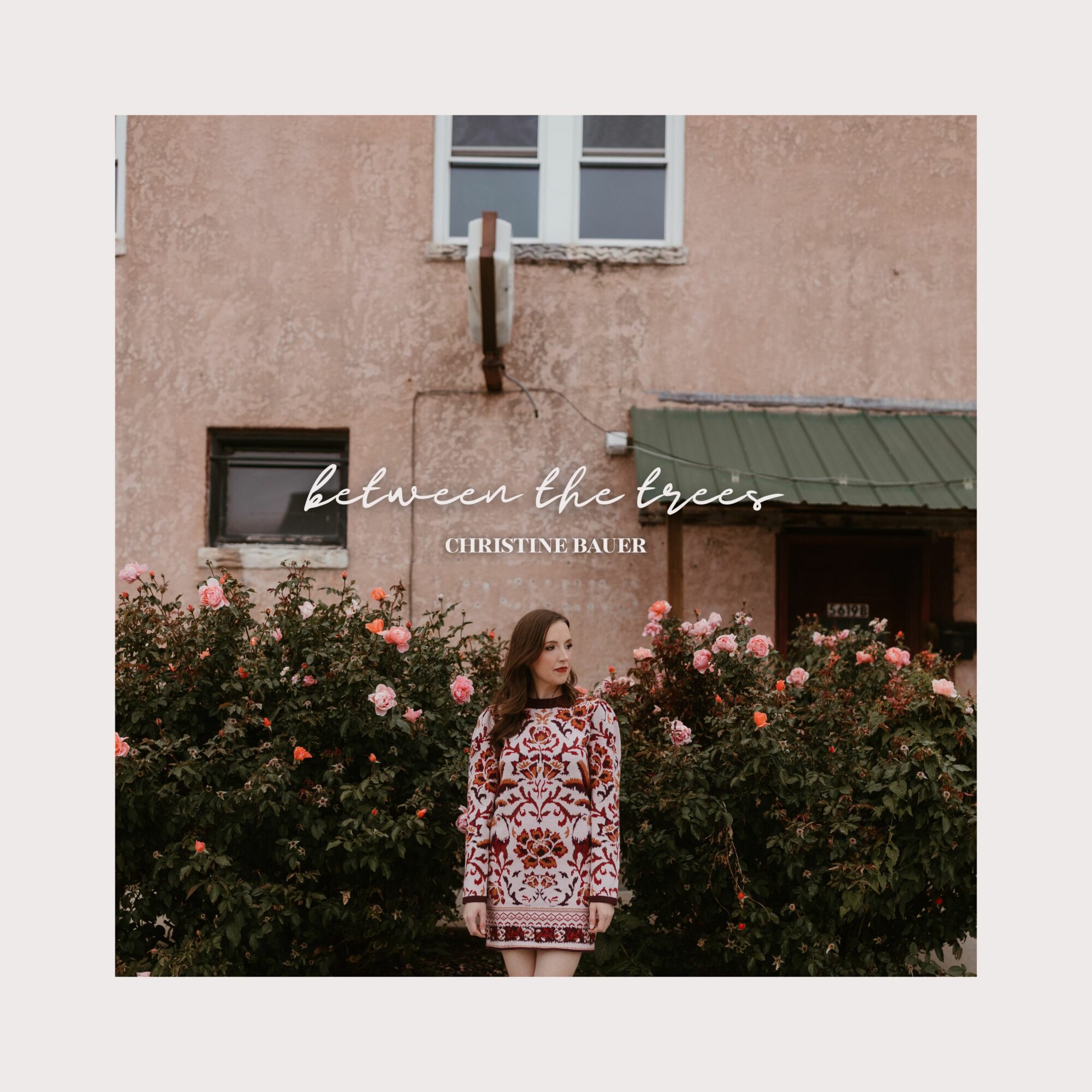 Young woman standing in front of pink building with pink flowers, text overlay reads 'between the trees' and 'christinebar'.