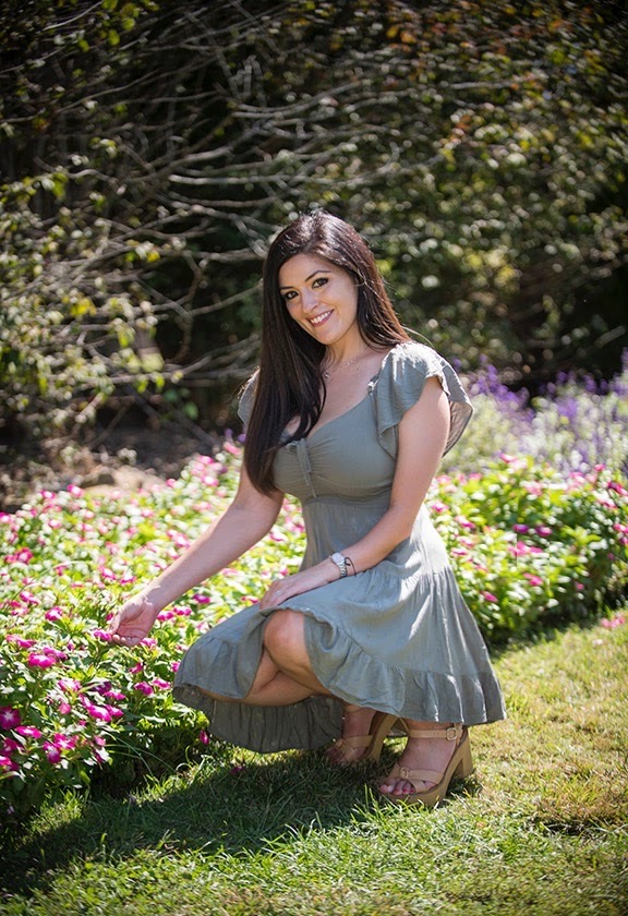 Young woman in a light blue dress crouching in a garden with colorful flowers and greenery.