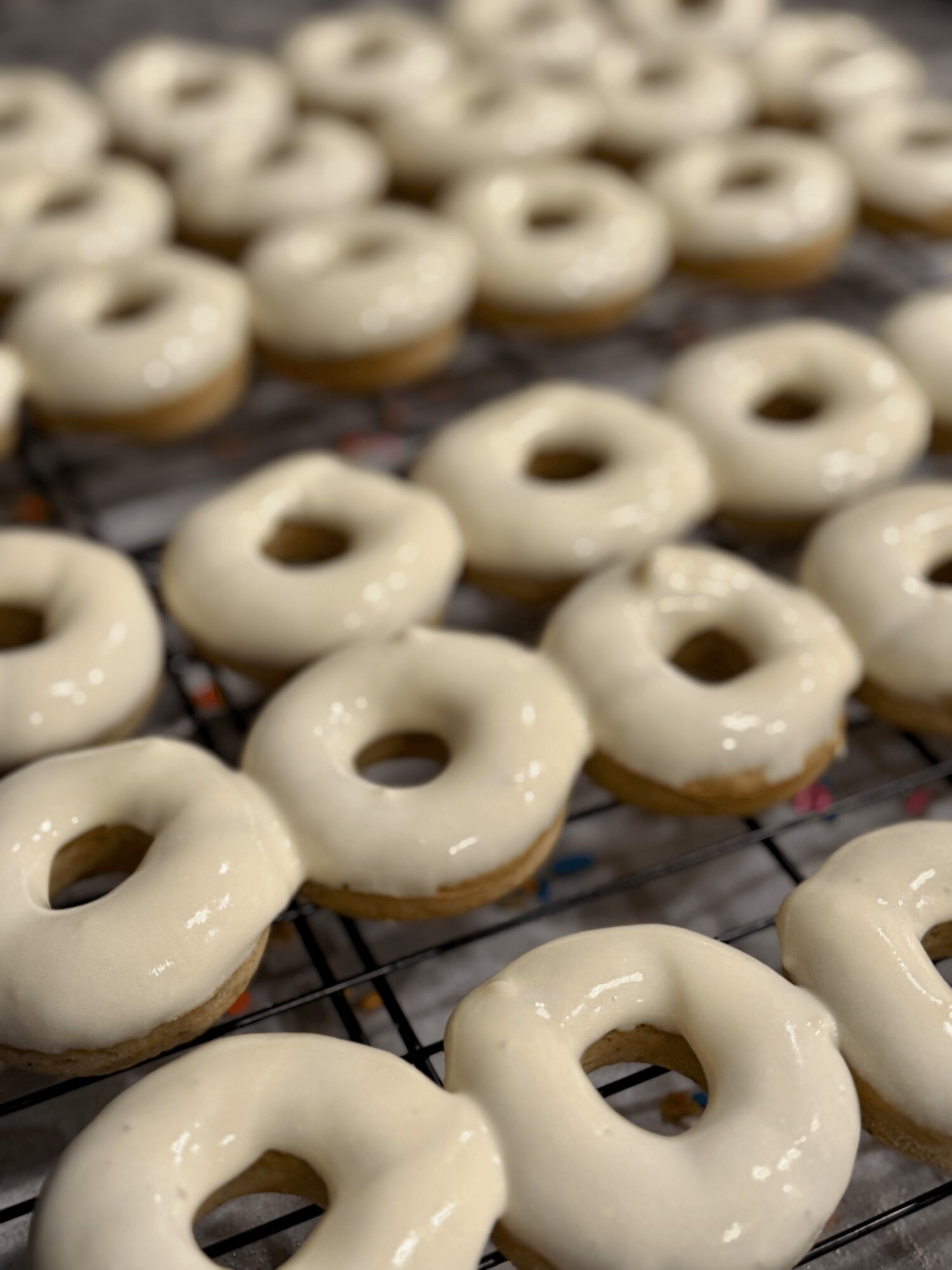 Many glazed donuts with a hole in the center are cooling on a wire rack.