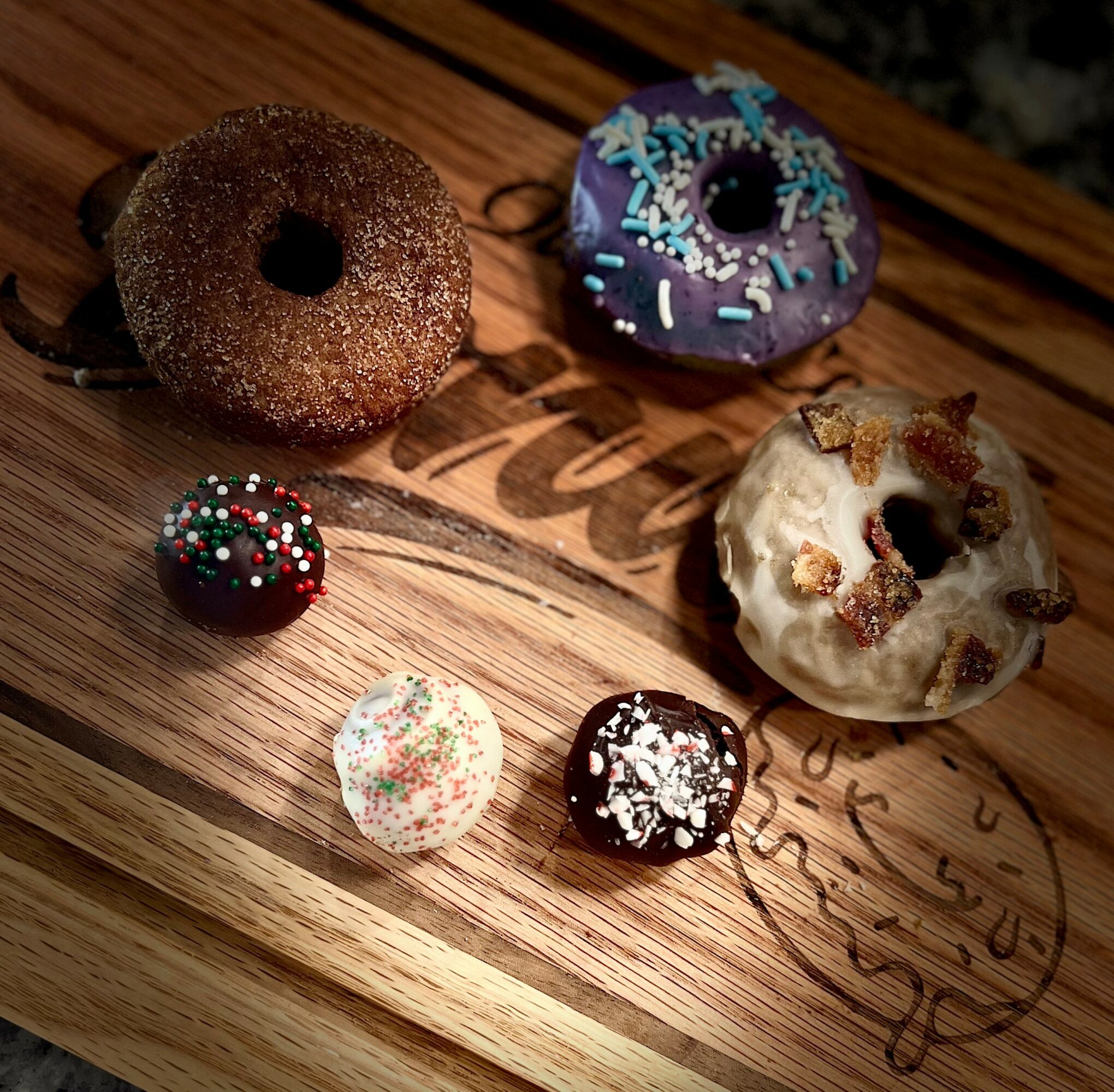 Six donuts and three cake pops on a wooden surface, with colorful sprinkles and toppings, some with holes, some whole.
