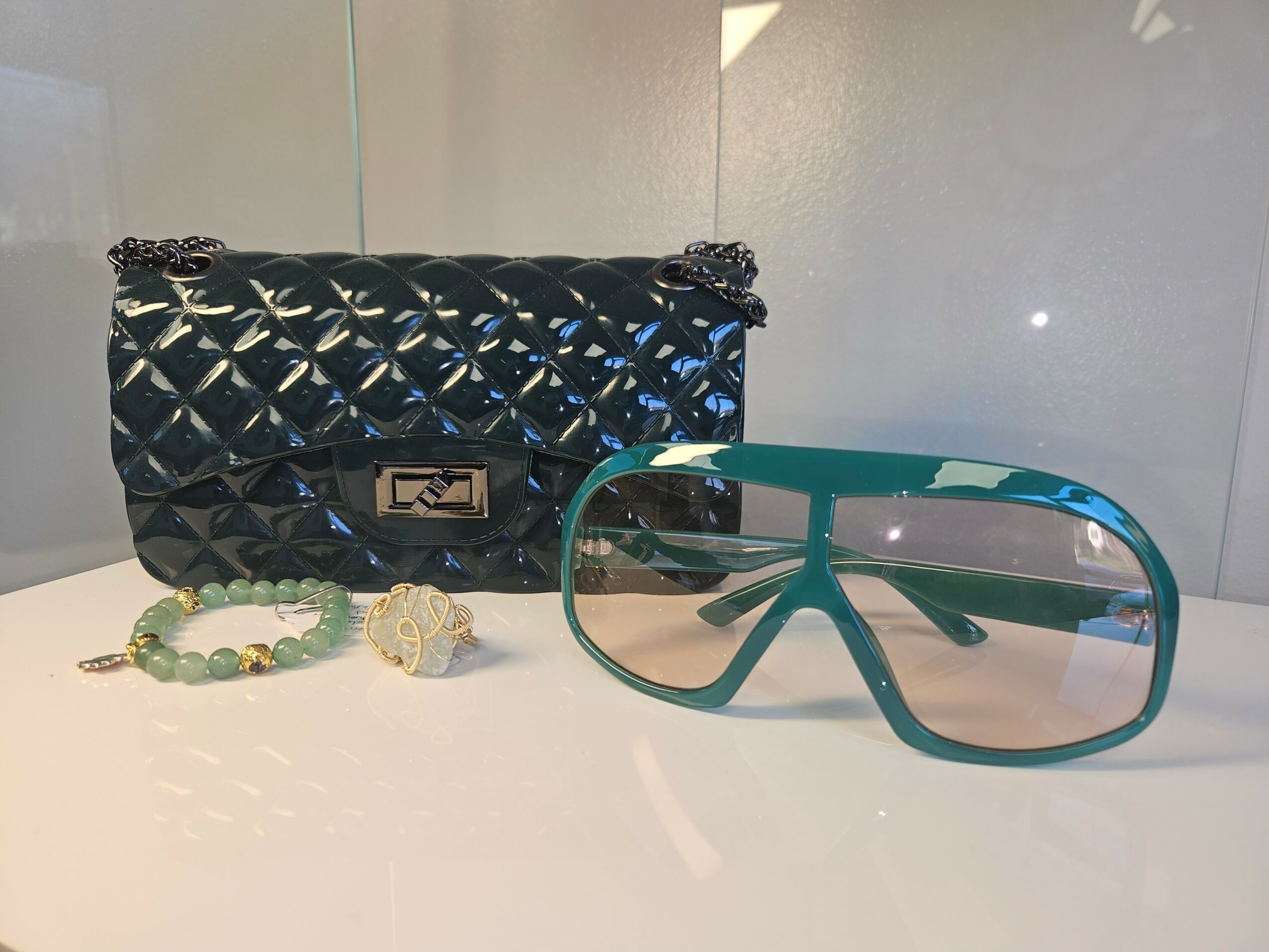 Black quilted handbag, sunglasses, and a beaded bracelet with a decorative element on a white surface.