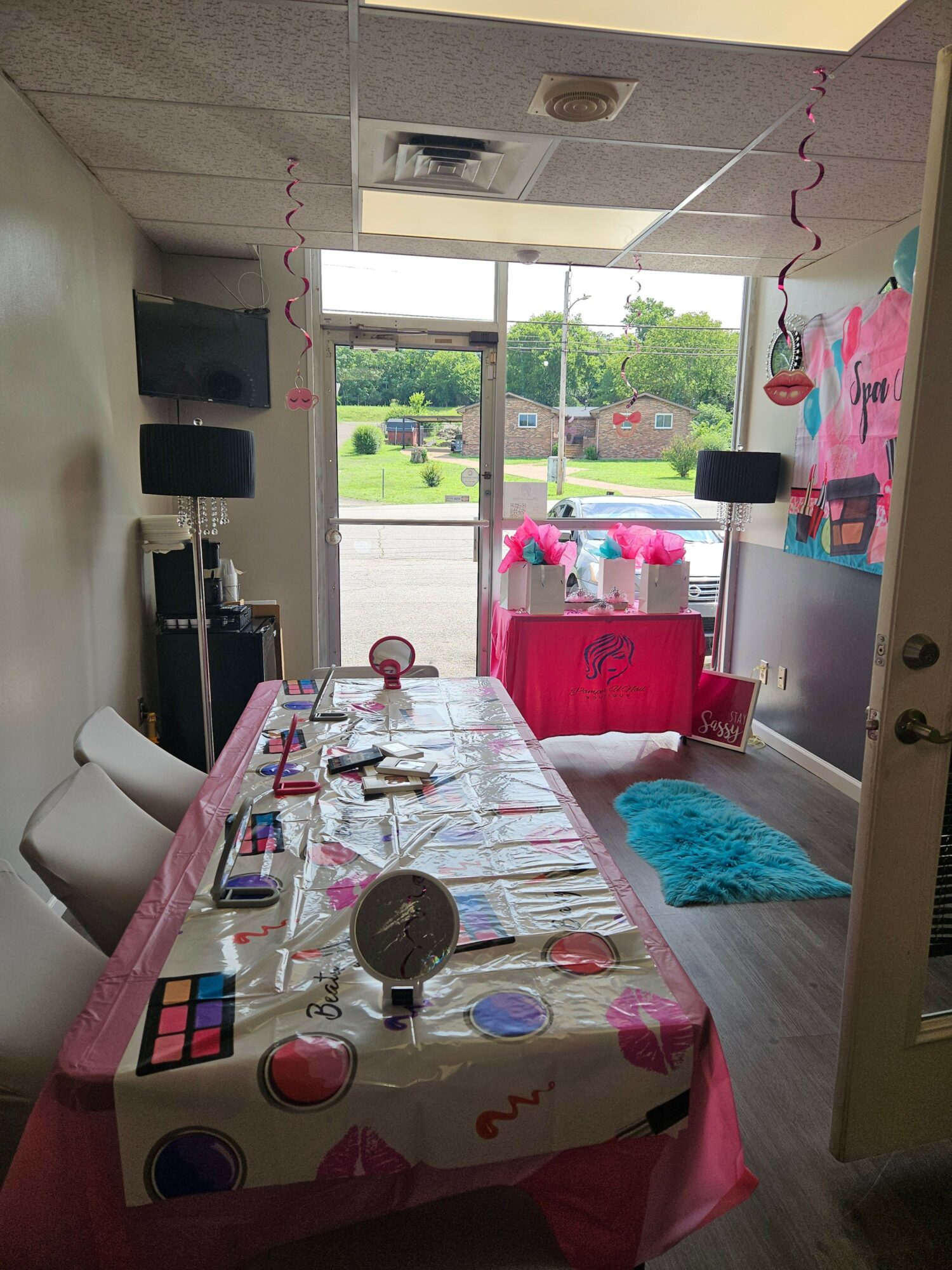 Party room with pink decorations, a table with a colorful tablecloth, and a window showing outdoor greenery.
