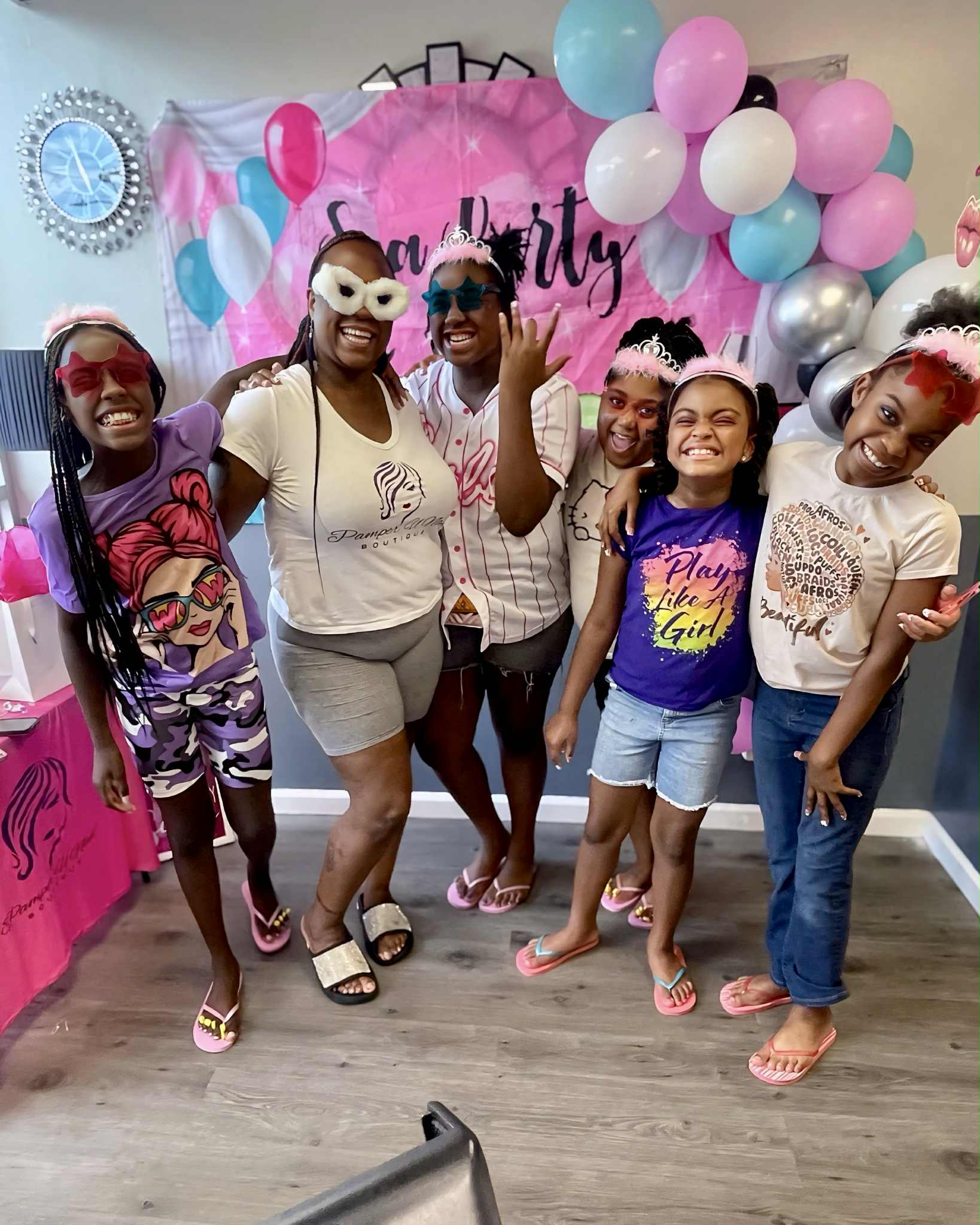 Group of six women and girls smiling at a party with pink, white, and blue balloons and a pink backdrop.