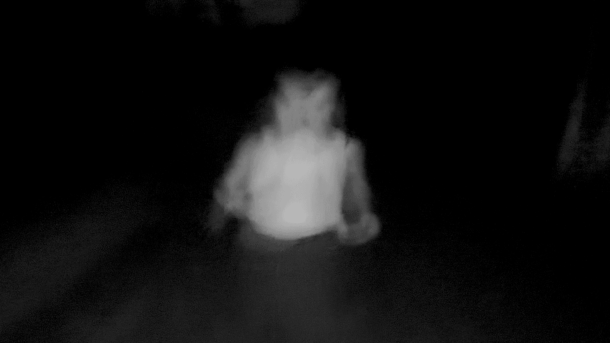 Person sitting in darkness, illuminated faintly, with blurred features, in a low-light environment.