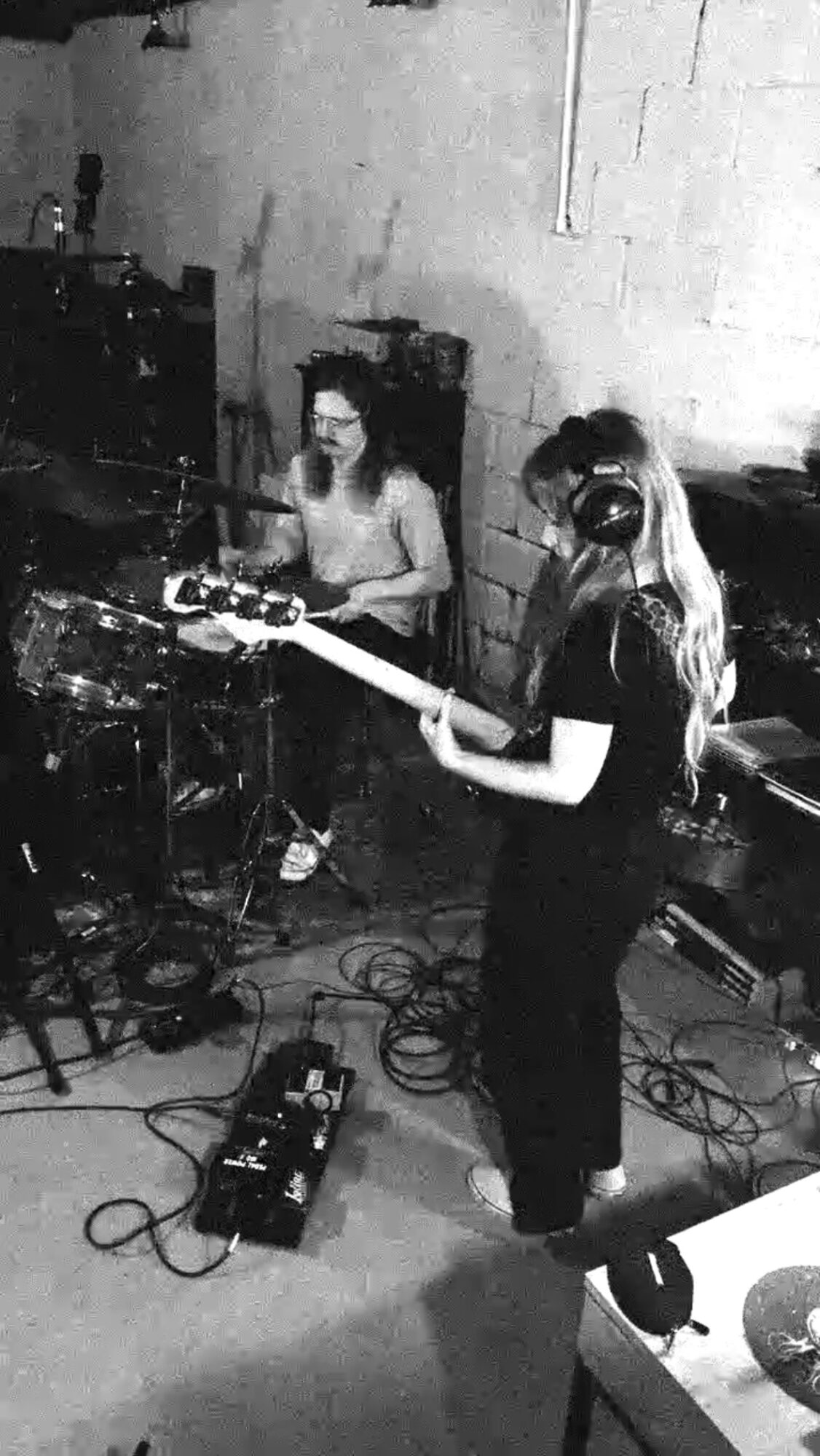 Two women in a music studio, one playing guitar and the other operating DJ equipment, with cables and equipment around them.