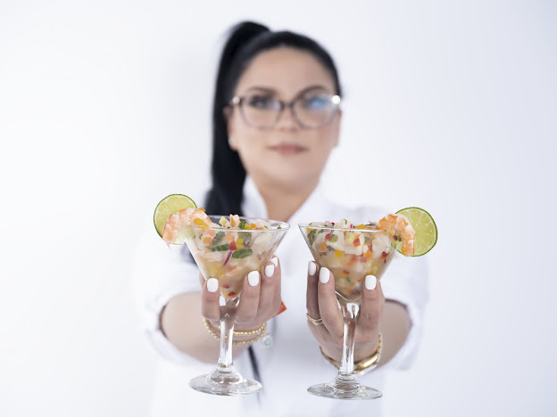 Person holding two cocktail glasses with lime slices, blurred background, wearing glasses and white shirt.