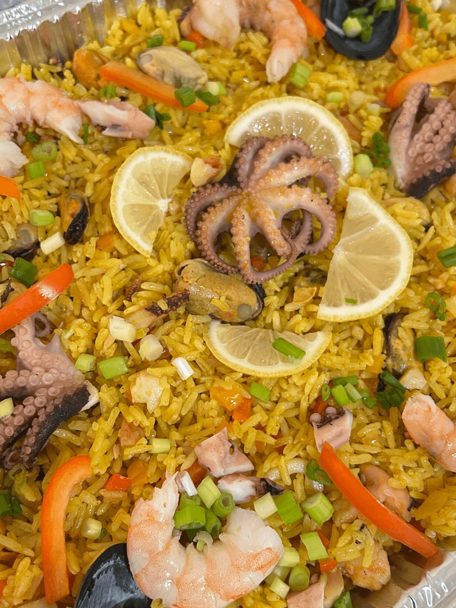 Seafood paella with shrimp, octopus, lemon wedges, and vegetables on yellow rice.