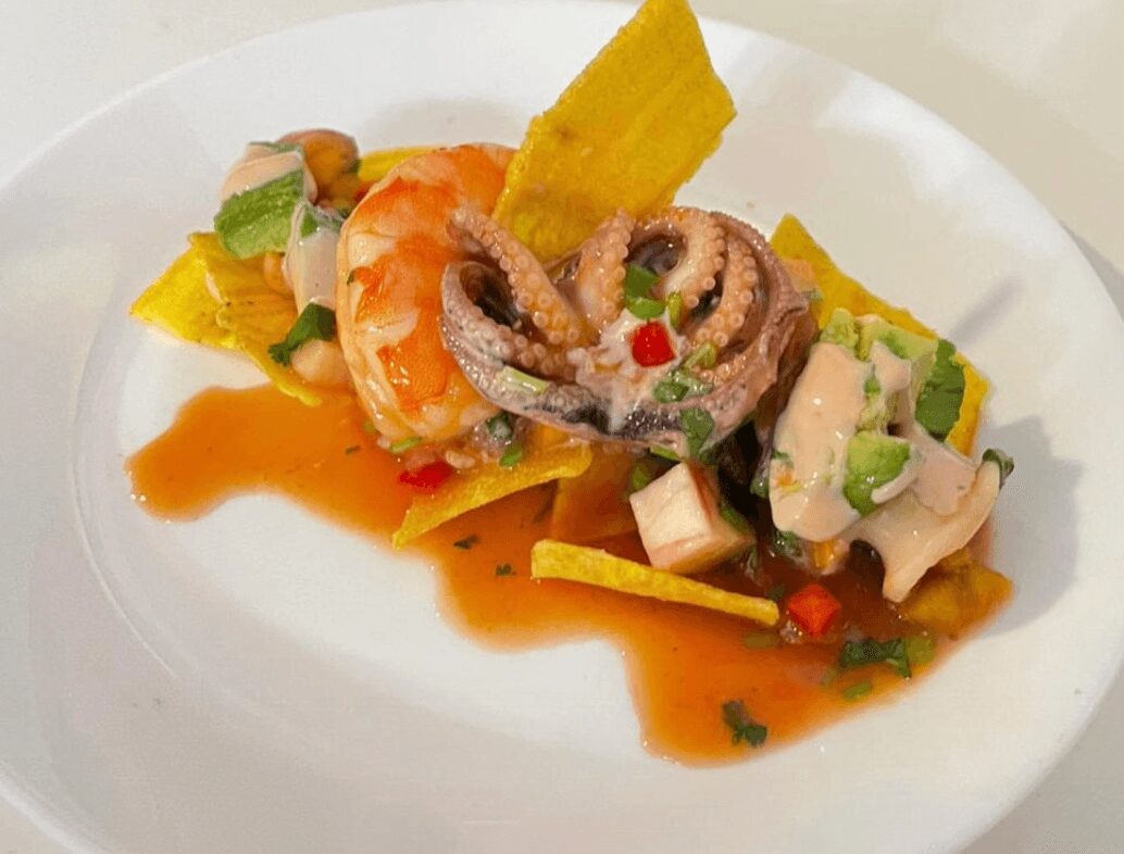 Seafood dish with shrimp, octopus, vegetables, and sauce on a white plate.