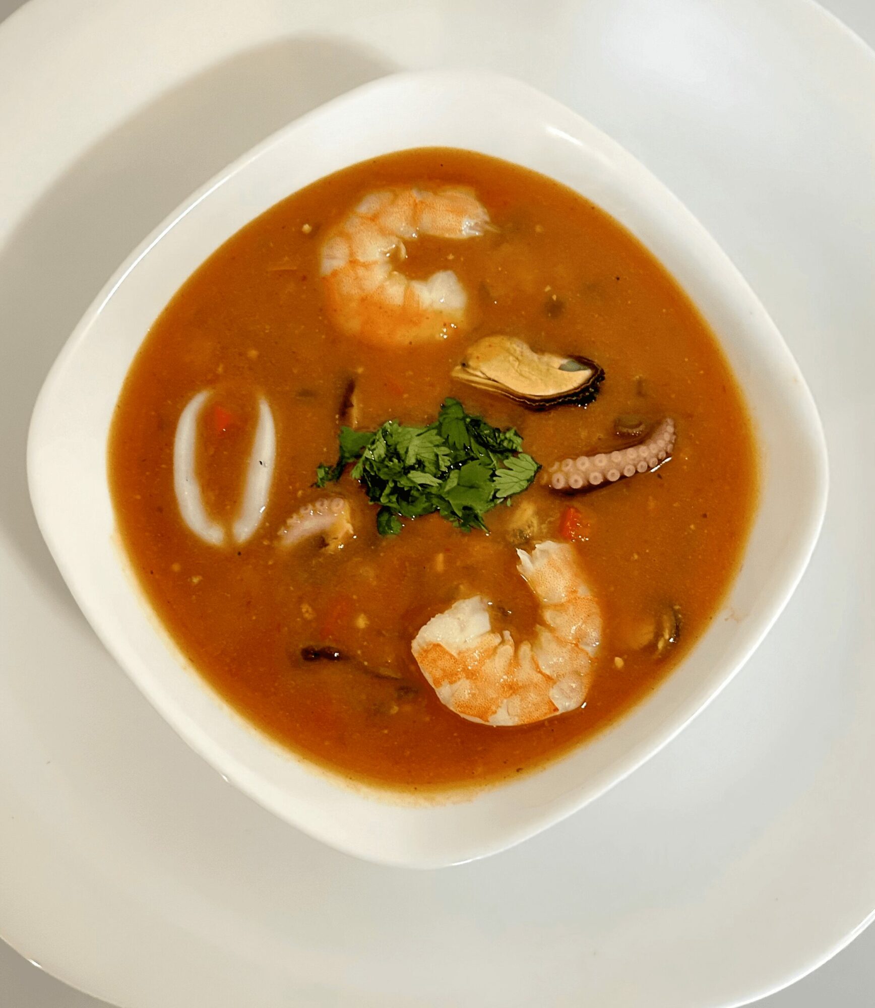 Bowl of seafood soup with shrimp, mussel, and herbs, served on a white plate.