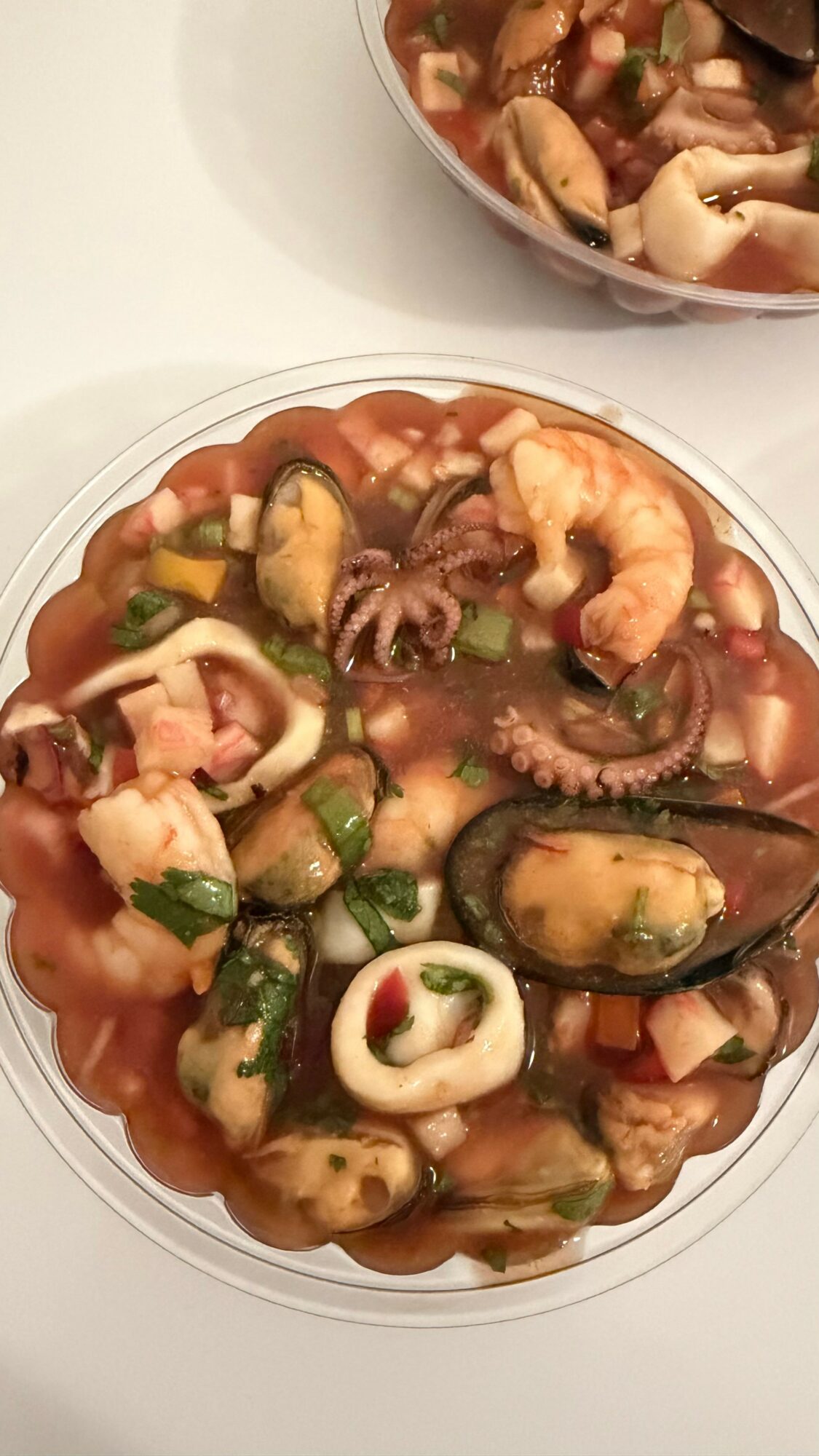 Seafood salad with shrimp, mussels, octopus, and vegetables in a clear bowl on a white surface.