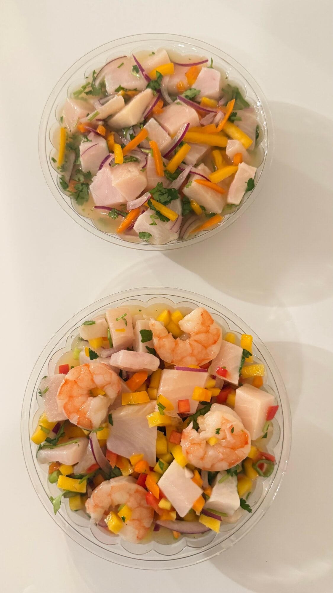 Two bowls of seafood salad with shrimp, fish, vegetables, and cheese on a white surface.