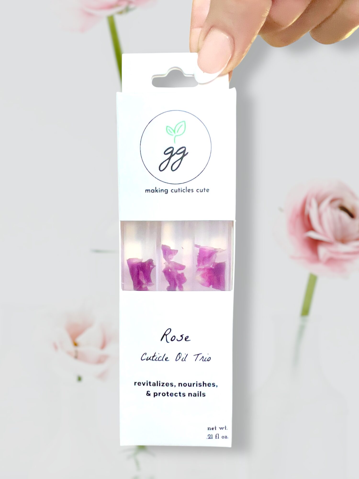 Hand holding a box of rose-shaped nail decorations with pink flowers in the background.