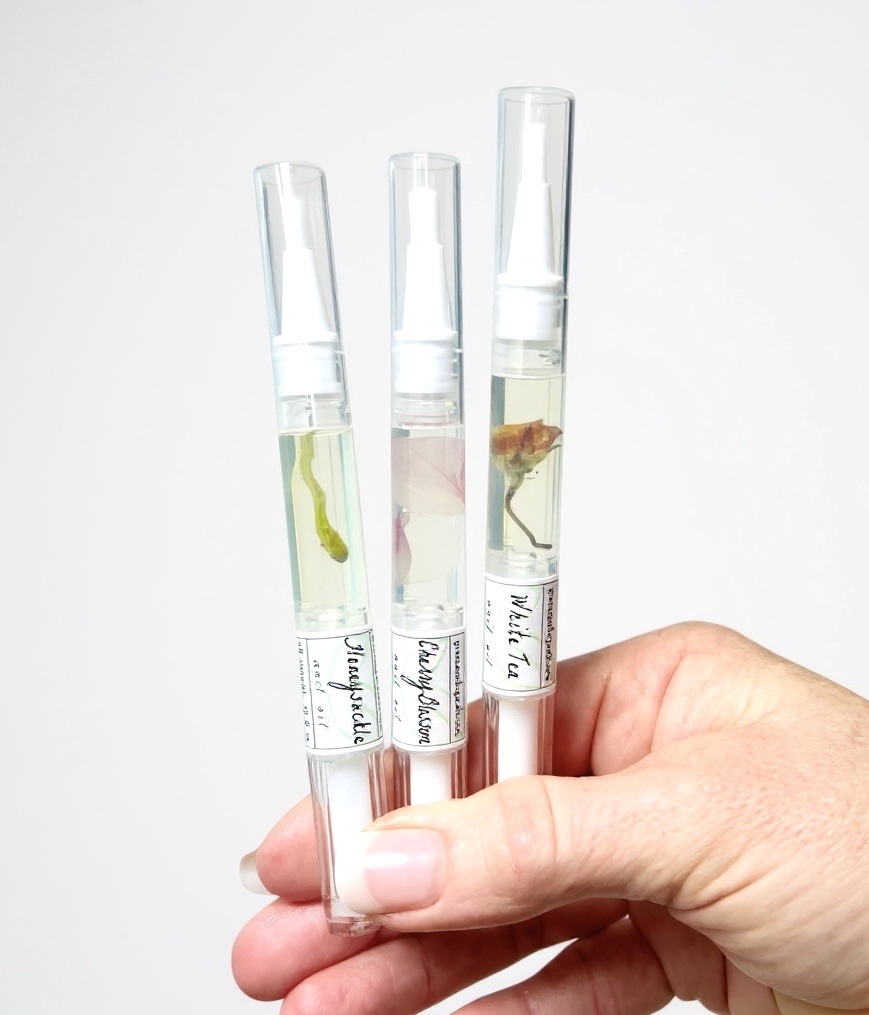 Hand holding three test tubes with liquid samples, labeled with handwritten tags, against a plain white background.