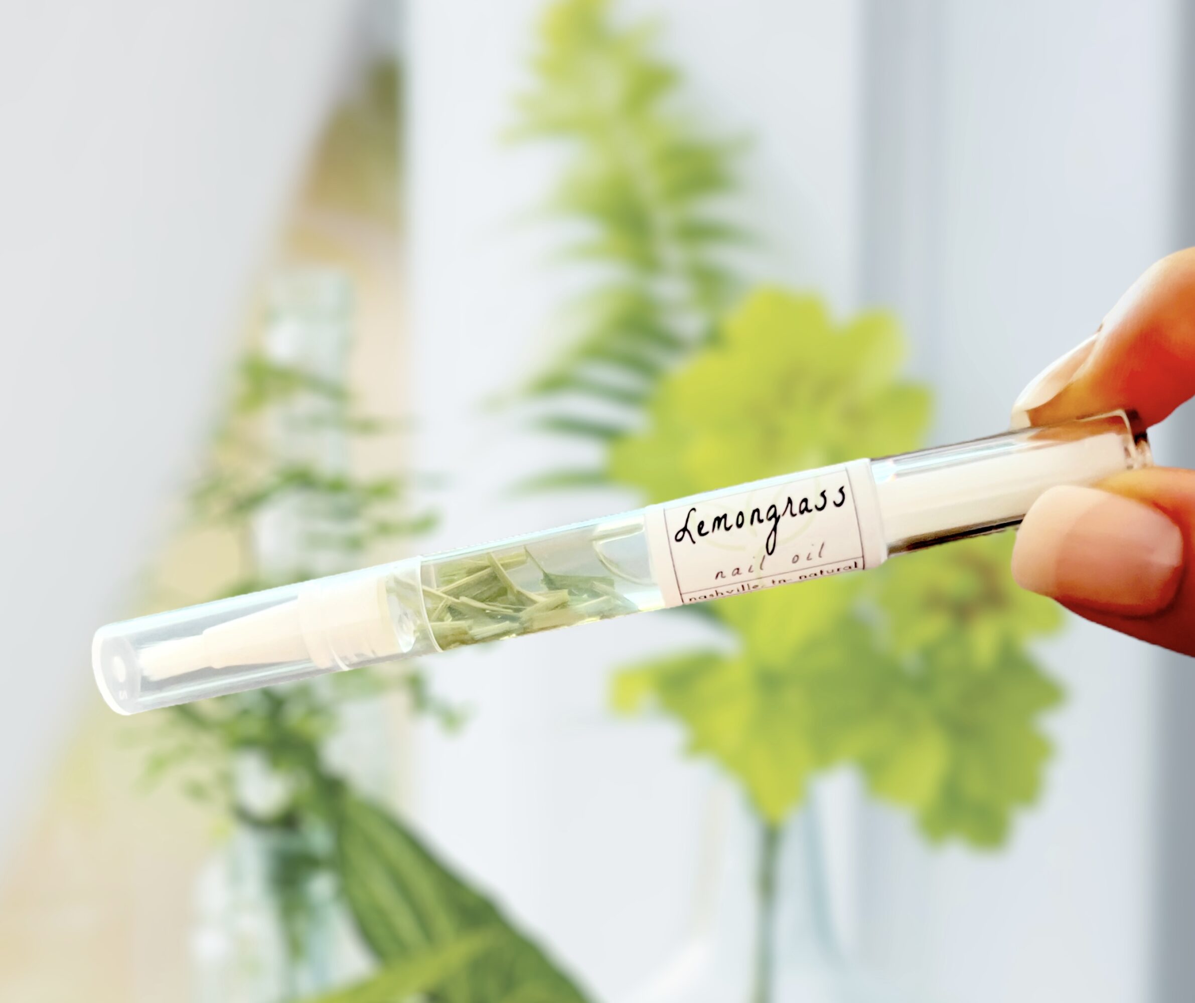 Person holding a test tube with a plant inside, labeled 'Lemongrass', in front of a window with green plants.