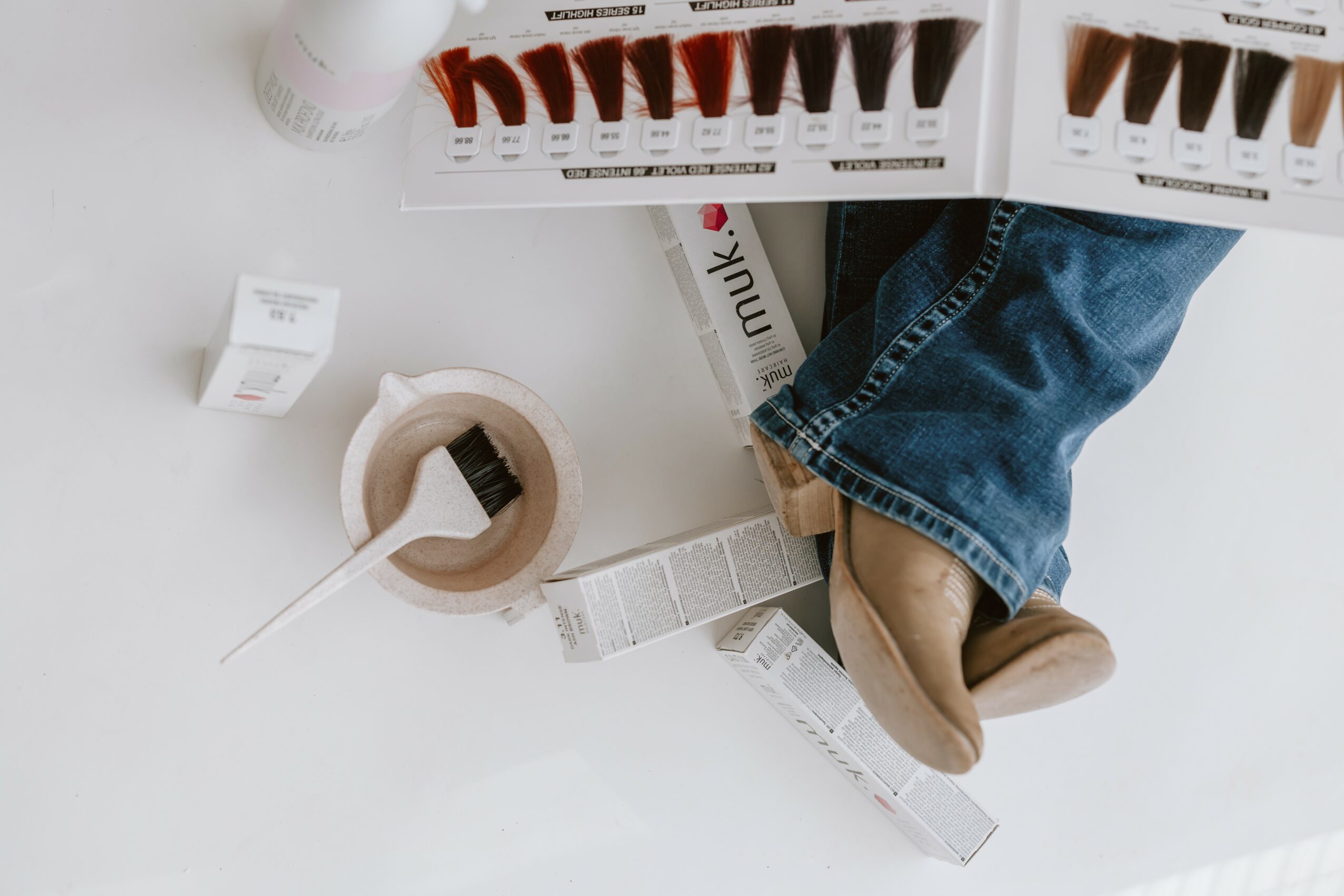 Person's legs and feet wearing jeans and beige shoes, surrounded by hair dye boxes and applicator, on a white surface.