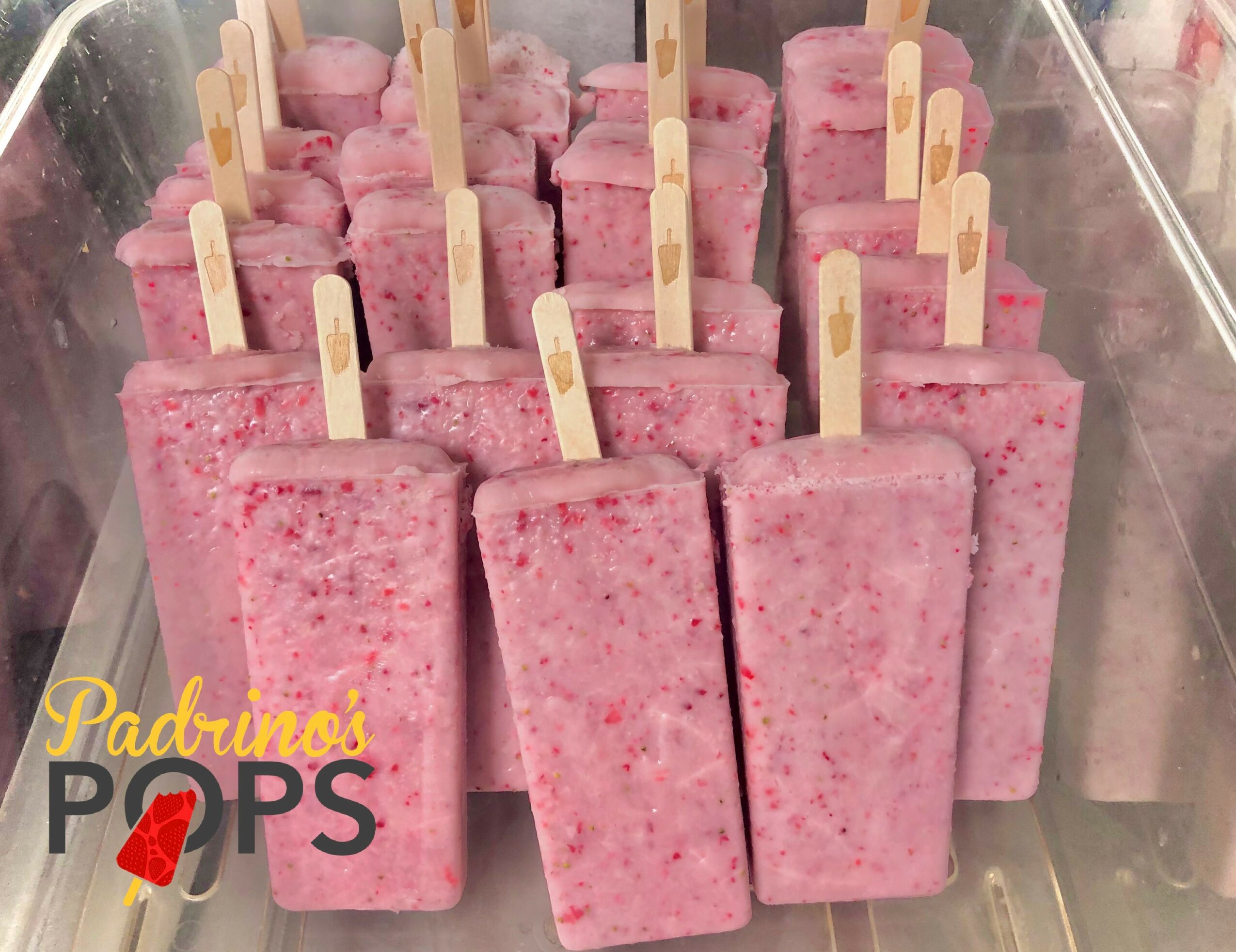 Pink popsicles with wooden sticks arranged in a tray, with a logo in the bottom left corner, 20 words.