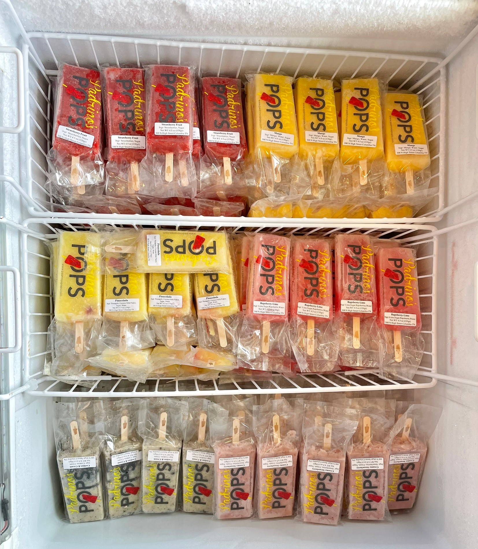 Inside a freezer, various Popsicle boxes are arranged on shelves, with different flavors and packaging colors visible.