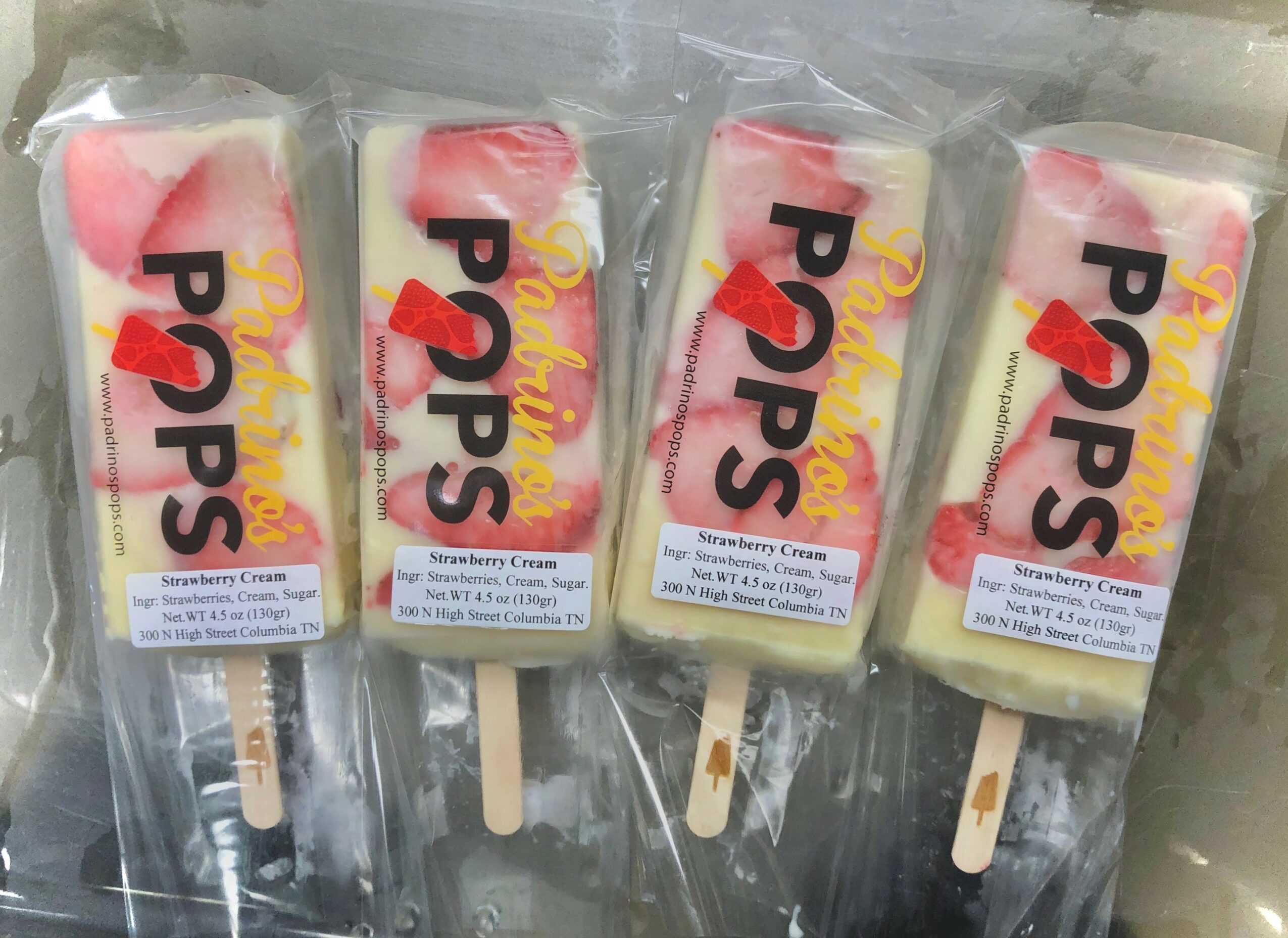Four popsicles with pink and white layers in clear packaging, labeled PPs, on a dark surface.