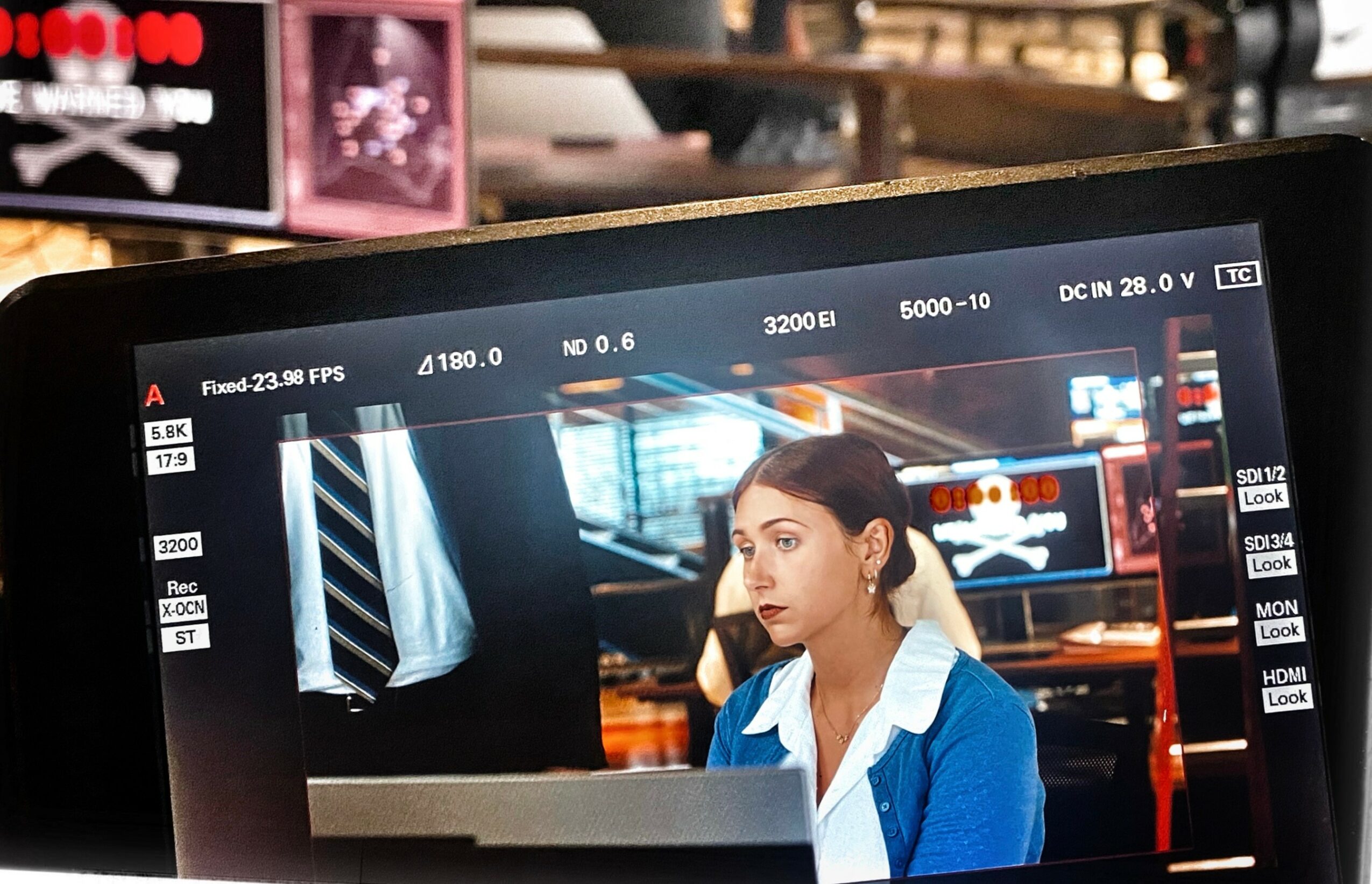 A woman with dark hair and a blue jacket sits at a desk in a modern office or studio setting.