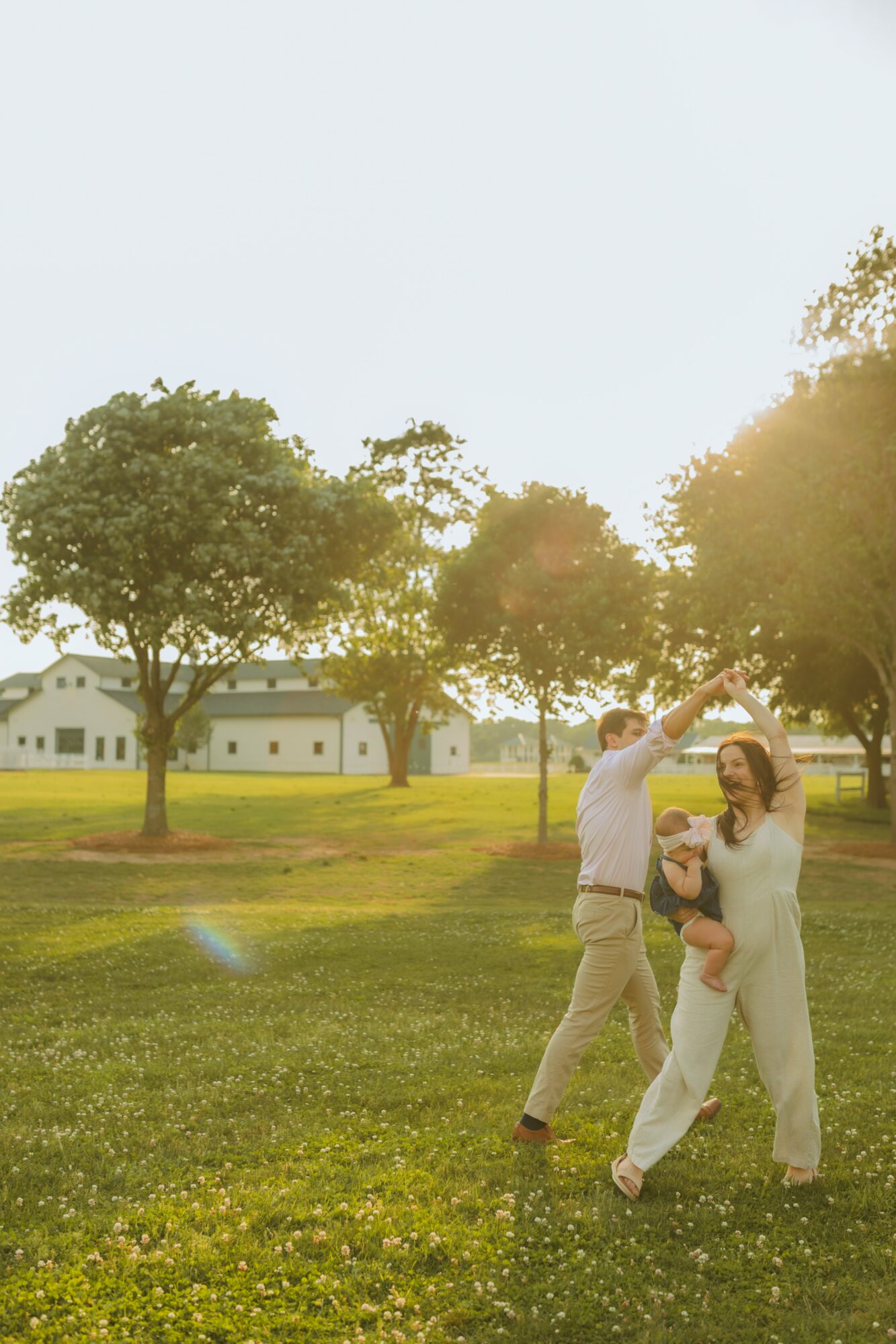 Two people dancing outdoors in a park with trees and a building in the background, sunlight shining through the trees.