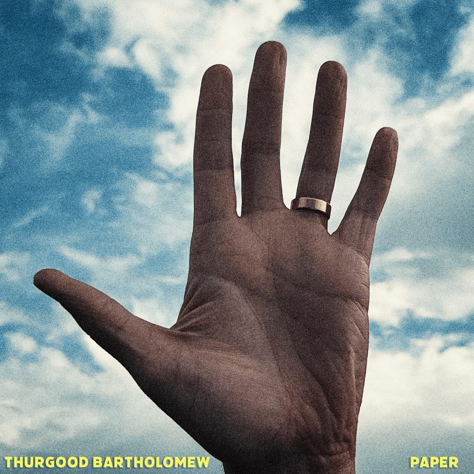 Hand with a ring on the middle finger raised against a cloudy sky background.