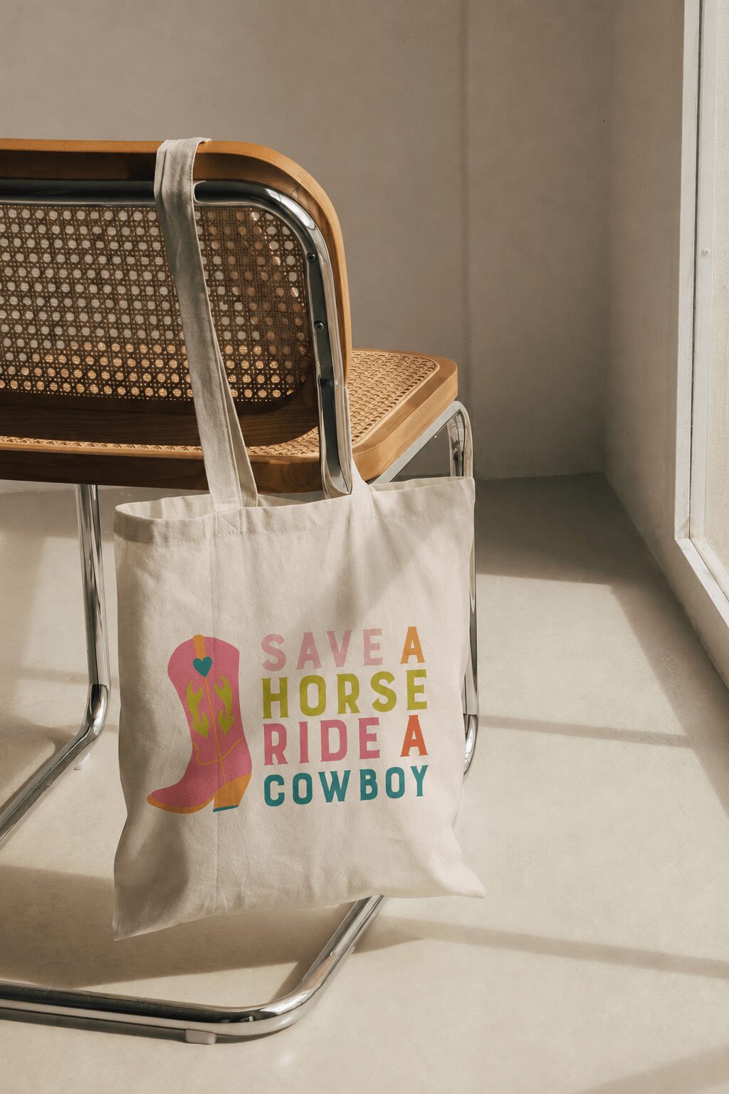 Canvas tote bag hanging on a chair, with colorful text about horse riding and cowboys, in a room with sunlight.