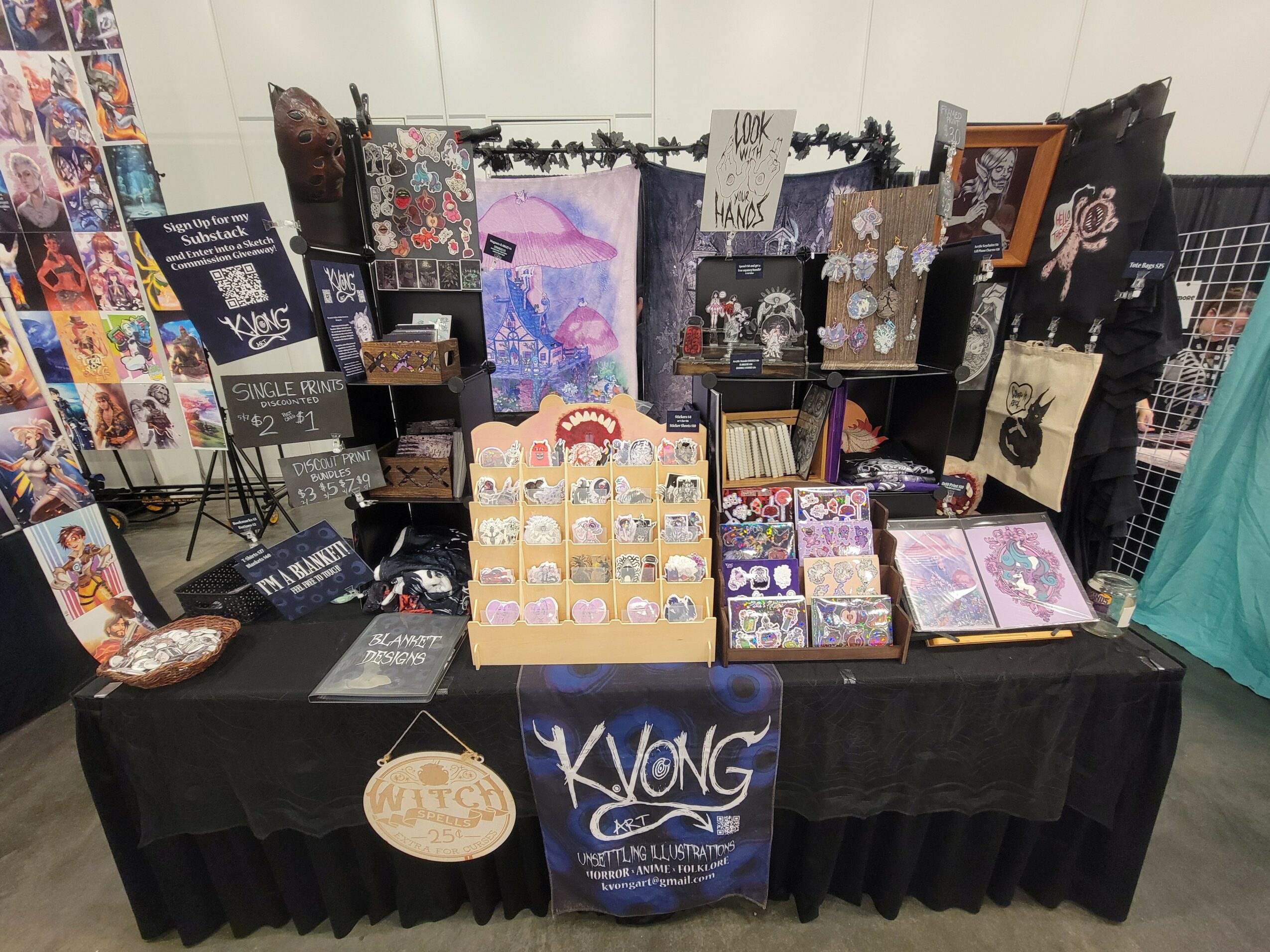 Display table with various artwork, cards, and crafts, arranged on black tablecloth with a backdrop of artwork and decorations.