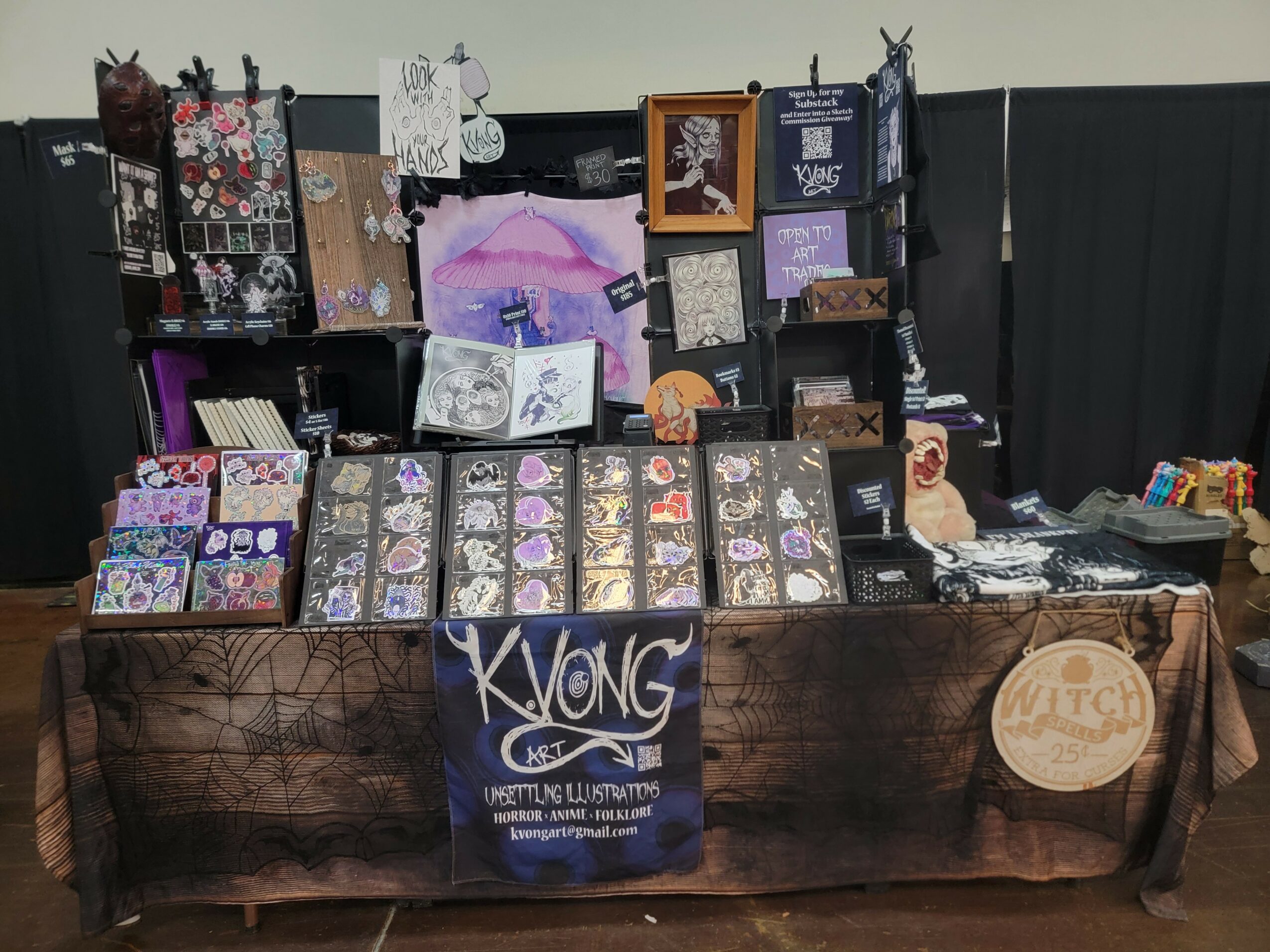 Display table with various jewelry and accessories, with a banner reading 'KYONG' in front, set against a black backdrop.