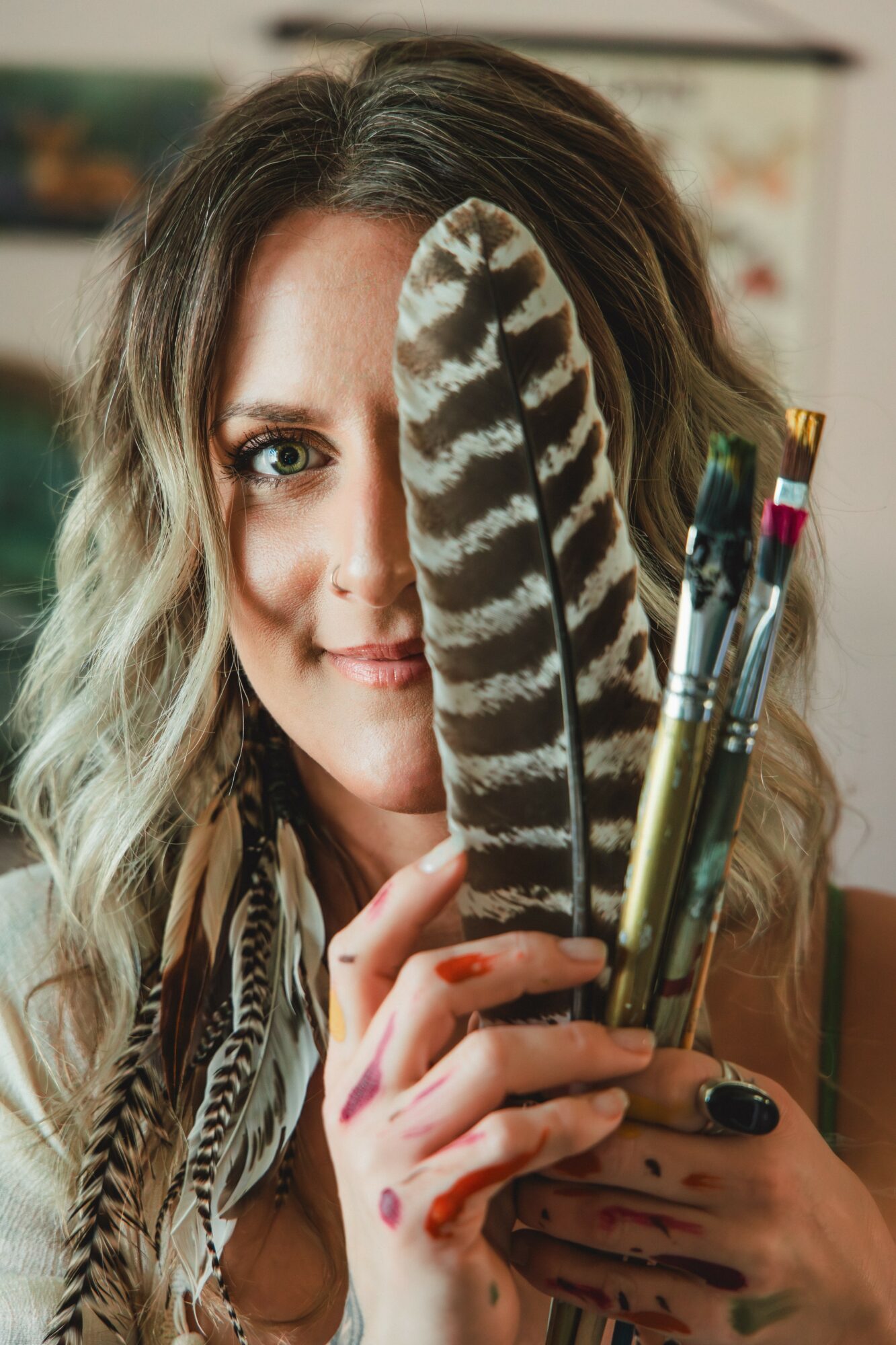 Woman with wavy hair holding a large striped feather and pens, partially covering her face, in an indoor setting.