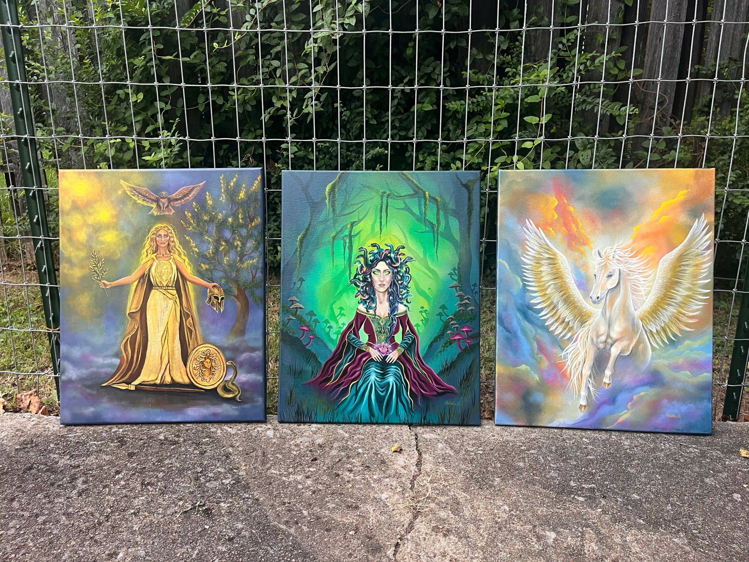 Three paintings of mythical and fantasy figures, including a woman with a snake and a glowing orb, a woman with a crown, and a winged creature, outdoors on pavement.