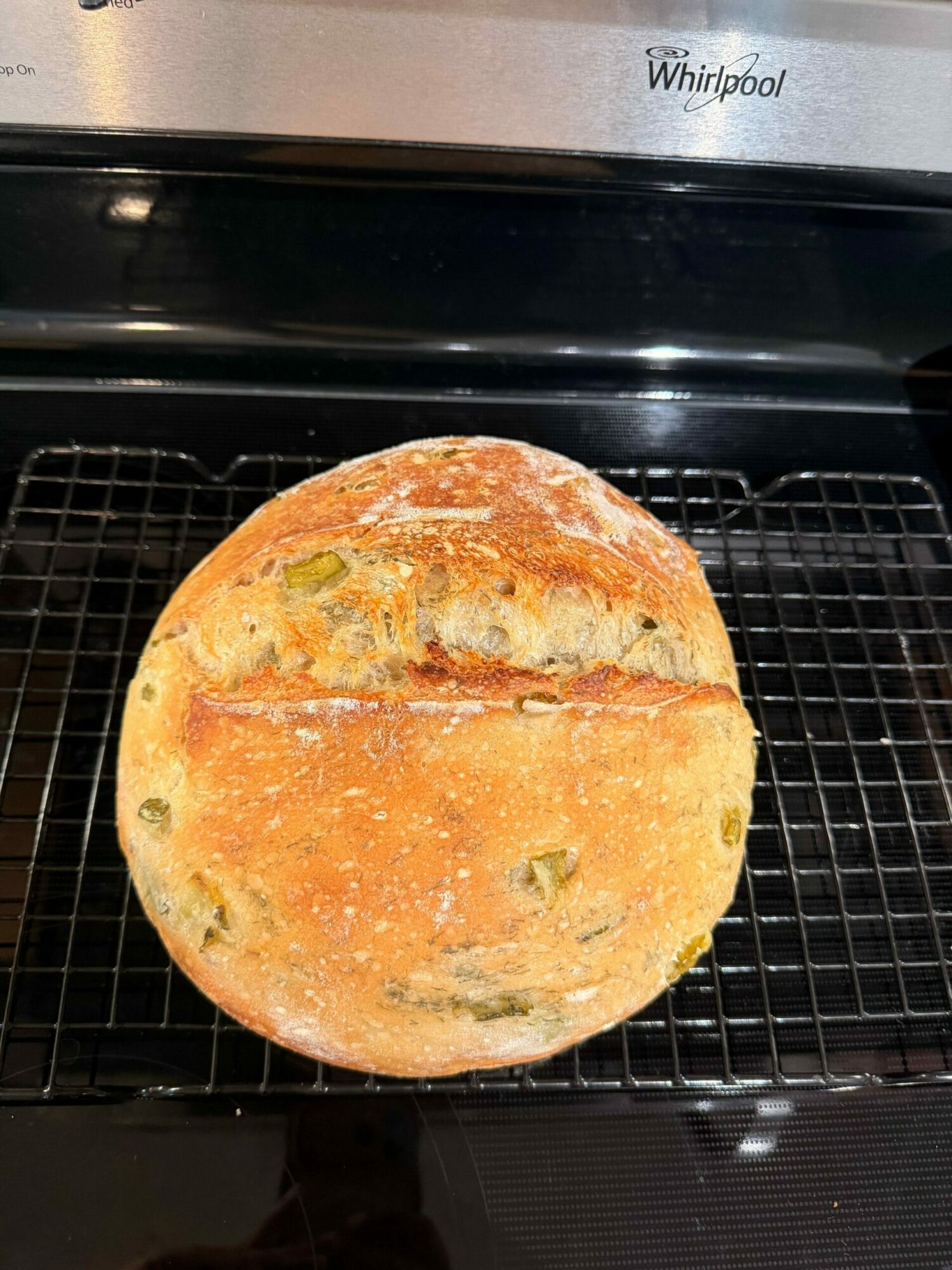 Round bread with a golden crust on a wire rack, with green bits inside, viewed from the side.