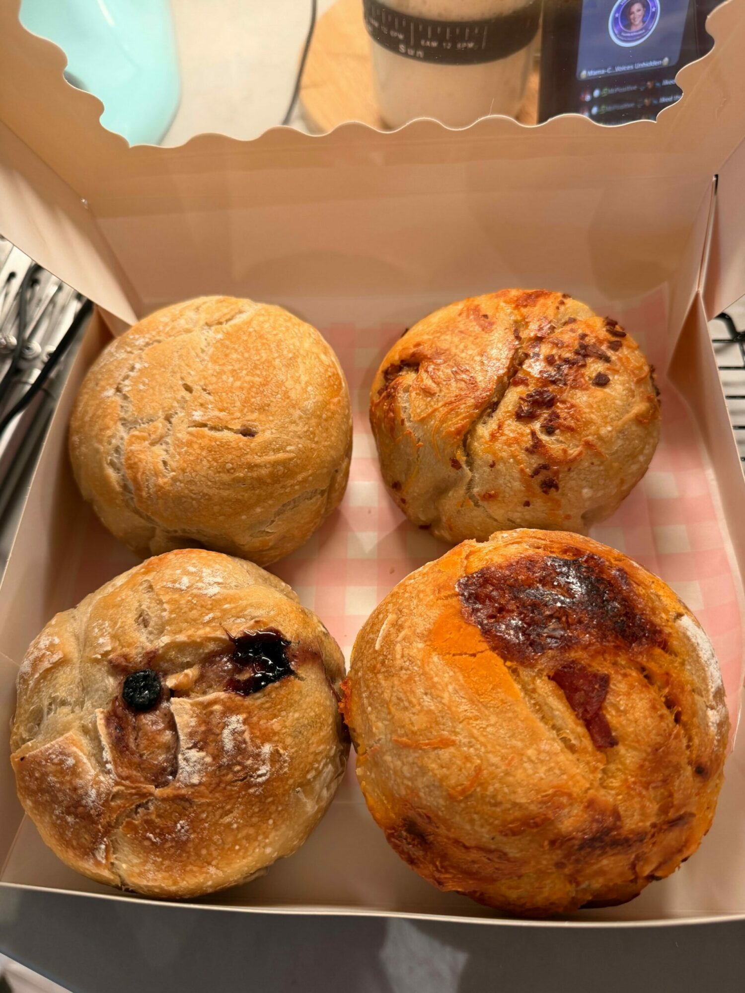 Four muffins in a box, two with chocolate chips, one plain, and one with a dark top, on a table.