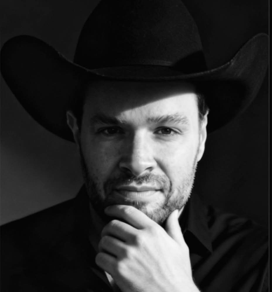 Man wearing a cowboy hat, resting his chin on his hand, in black and white.
