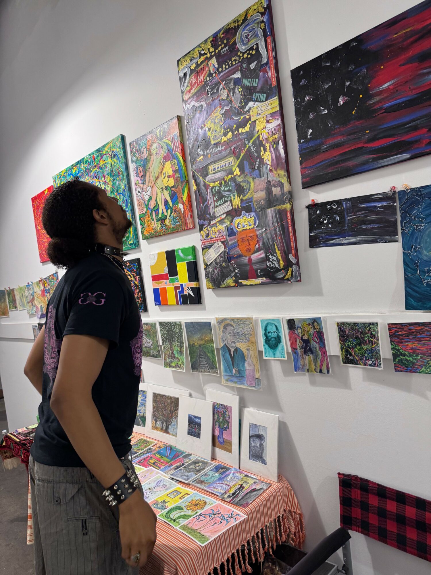 Person standing in front of colorful artwork and paintings displayed on white walls and tables.